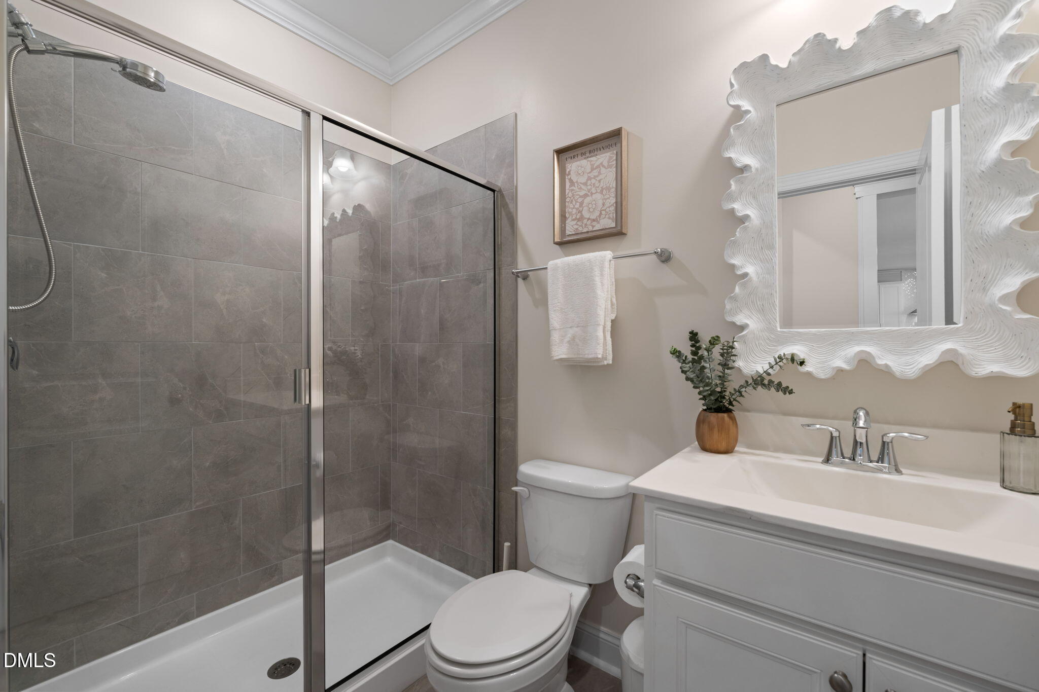 Bathroom with a gray-tiled glass shower, white vanity, and sculptural white-framed mirror.