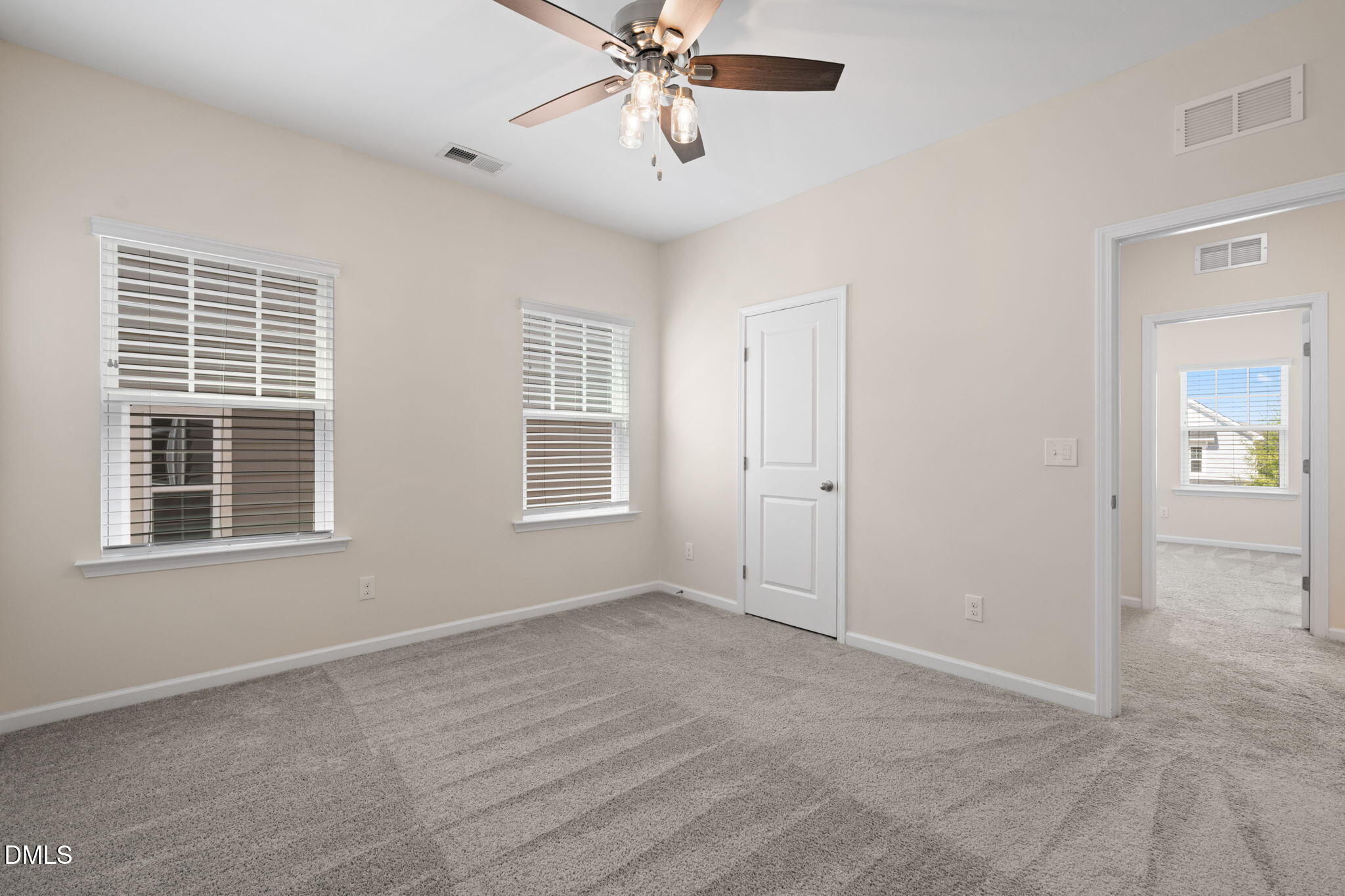 Empty carpeted bedroom with two windows, a ceiling fan, and a doorway to another room.