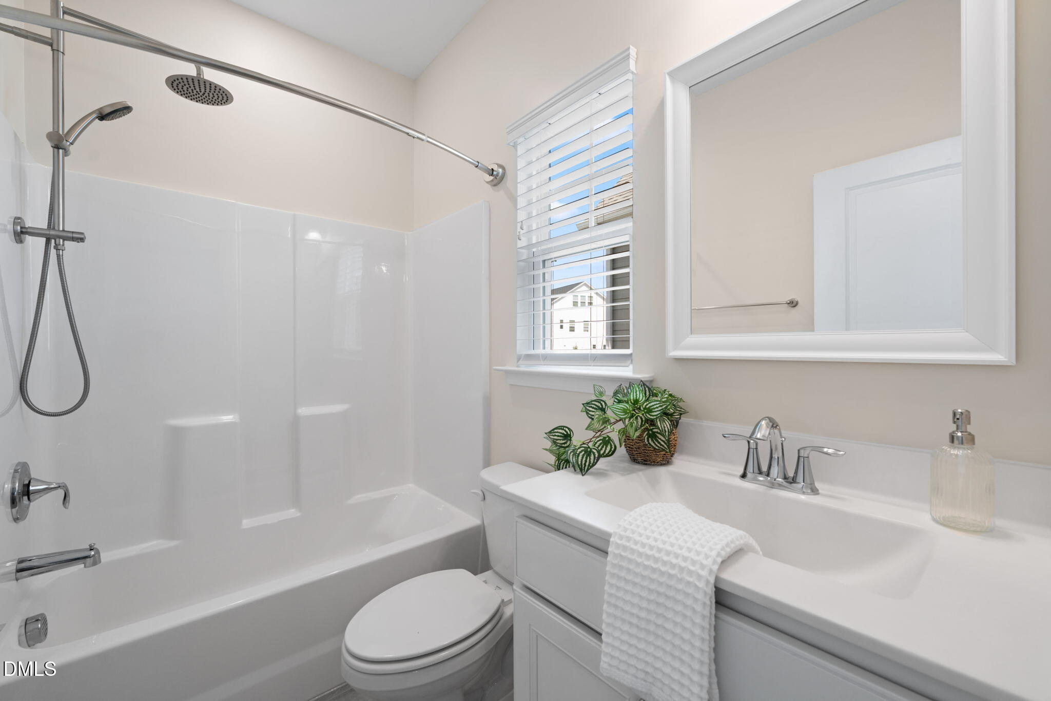 Bathroom with white tub and shower, chrome fixtures, and a vanity beneath a window with blinds.