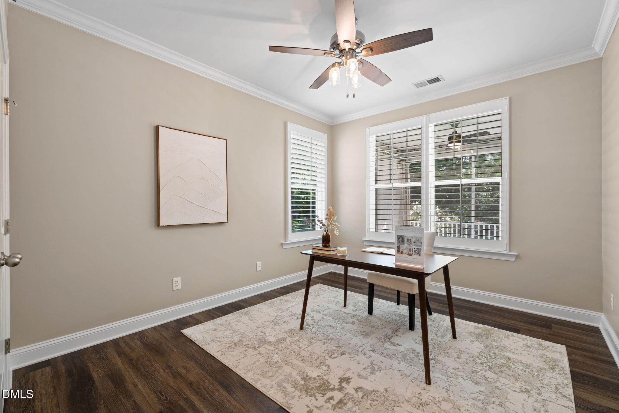 Home office with a dark wood desk, plantation shutters, and a ceiling fan.