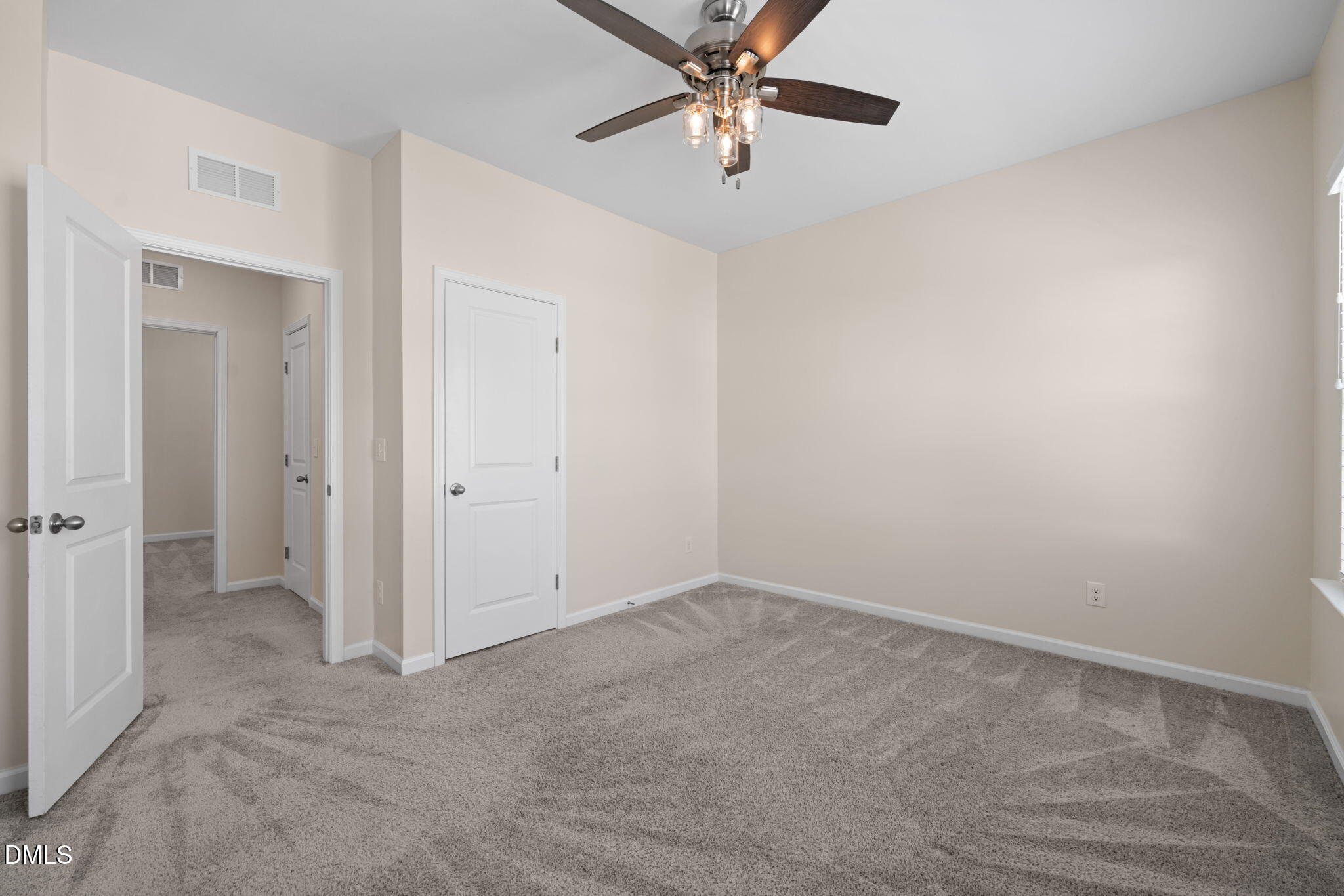 Empty bedroom with gray carpet, beige walls, and a ceiling fan with lights.