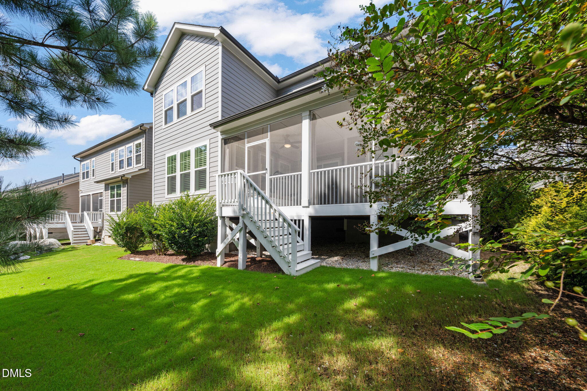 Gray two-story home with a screened porch, raised deck stairs, and shaded lawn.
