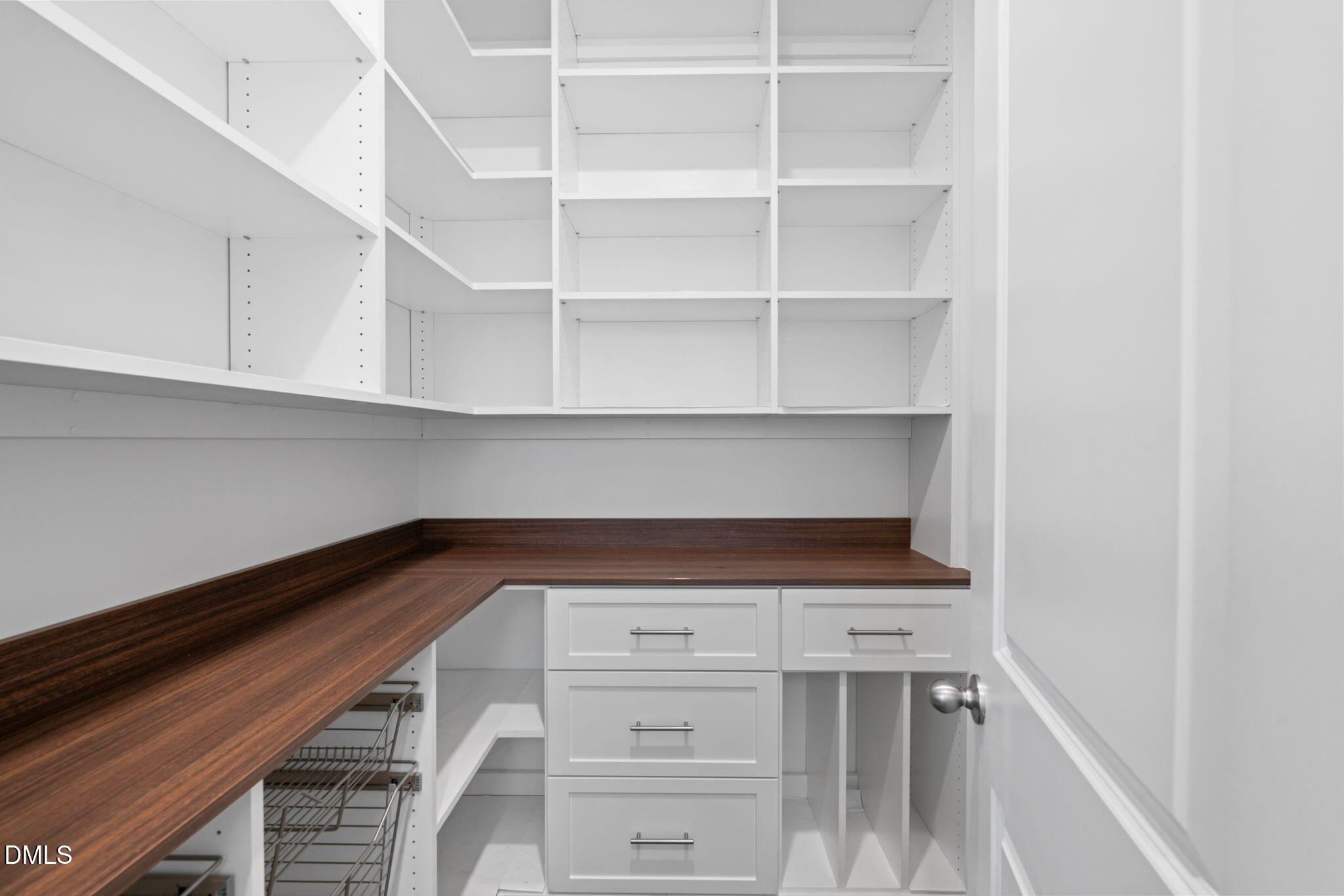 Built-in pantry with white shelving, dark wood countertops, drawers, and pull-out wire baskets.