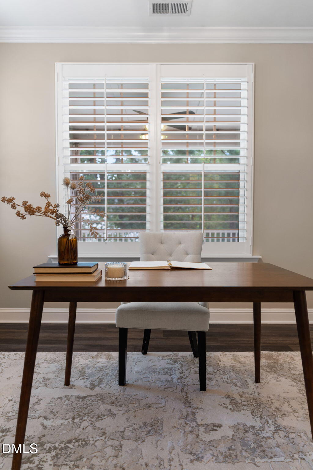 Staged home office with a dark wood desk and white-shuttered window.
