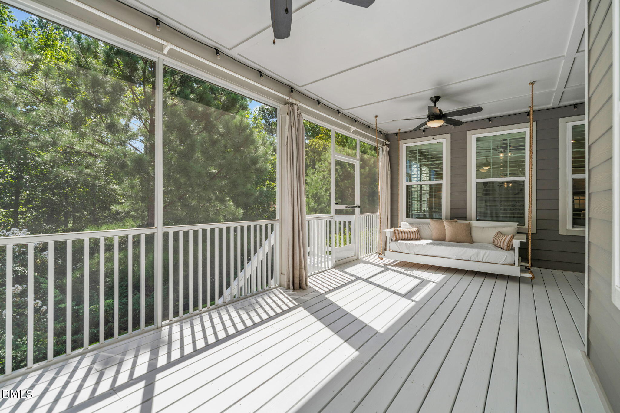 Screened porch with a cushioned swing, white plank floor, and leafy trees beyond the railing.
