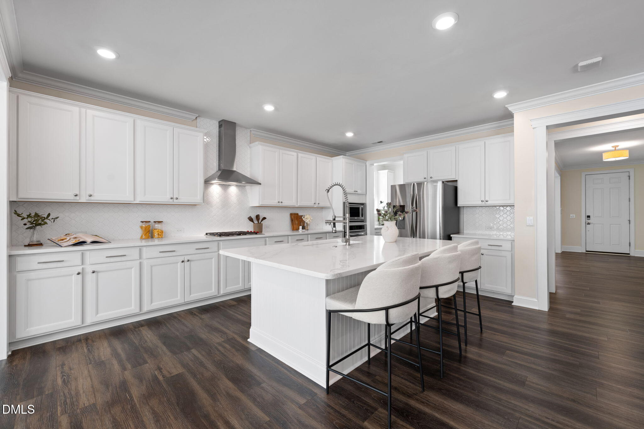 White kitchen with a large island, three bar stools, stainless steel appliances, and dark wood flooring.