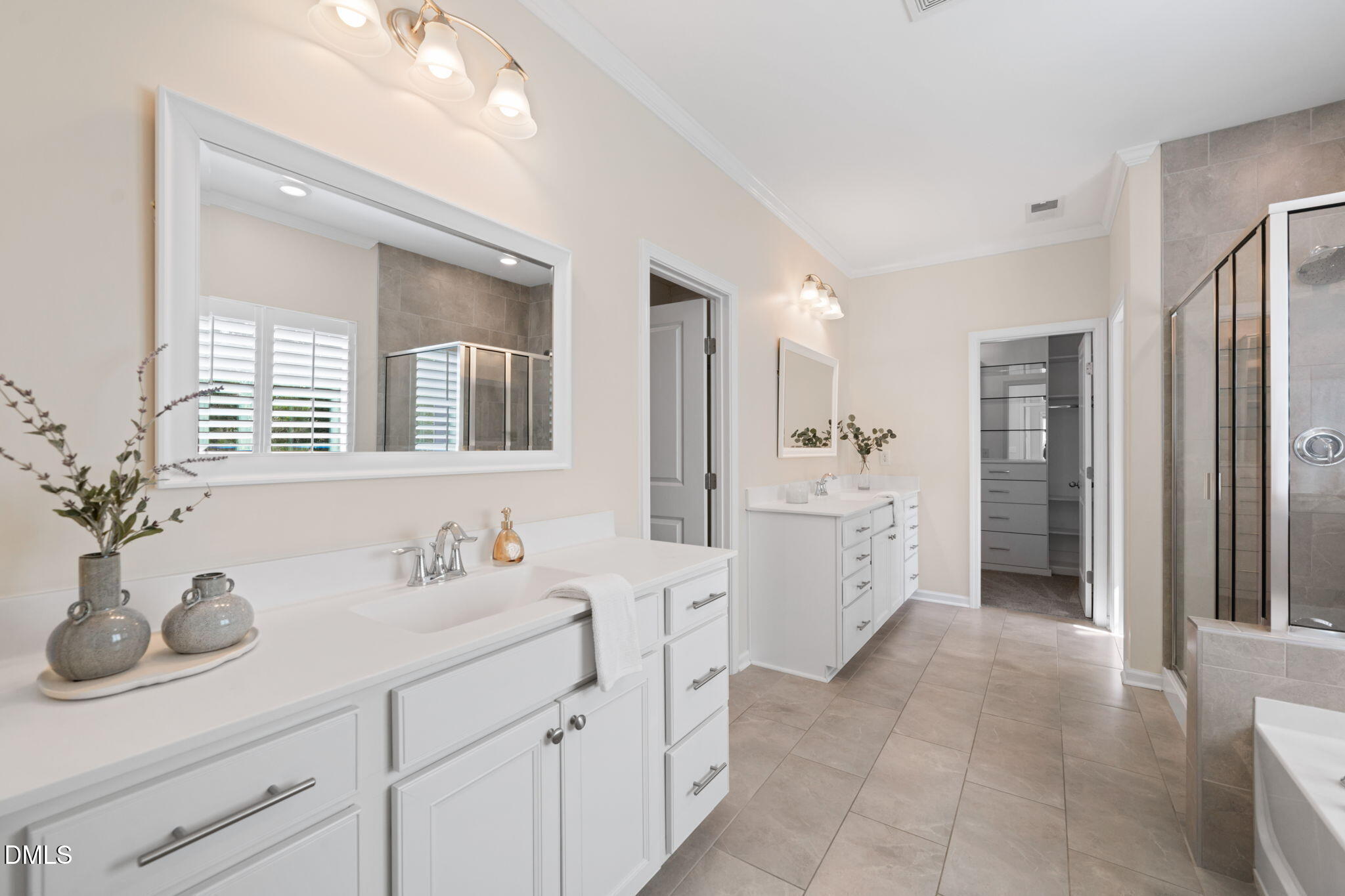Primary bathroom with dual white vanities, gray tile floors, and a glass-enclosed shower.