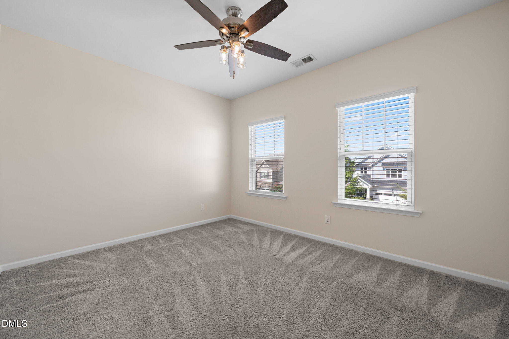 Empty carpeted bedroom with two windows and a ceiling fan.