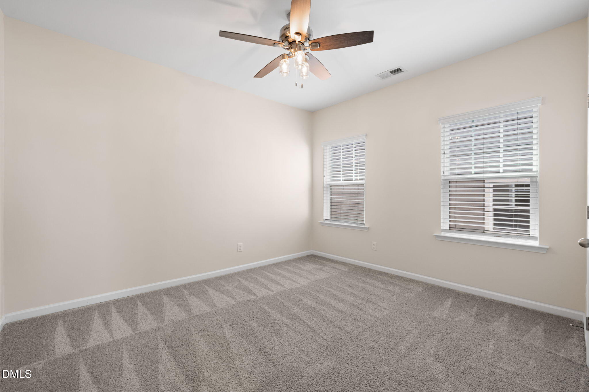 Empty bedroom with gray carpet, two blinded windows, and a ceiling fan.