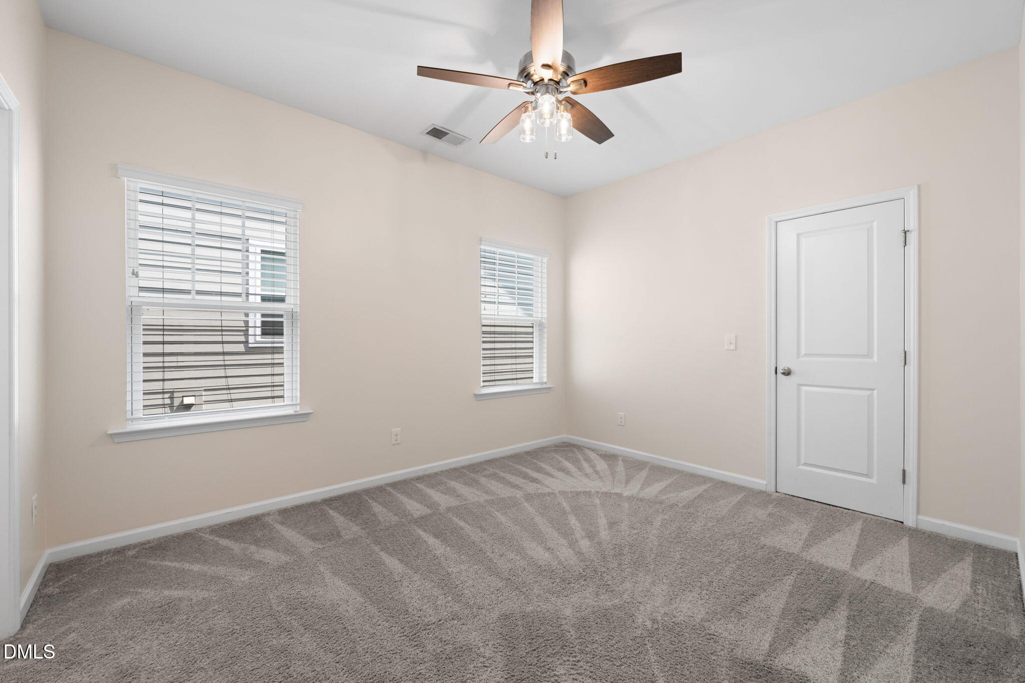 Empty bedroom with gray patterned carpet, two blinded windows, and a ceiling fan.