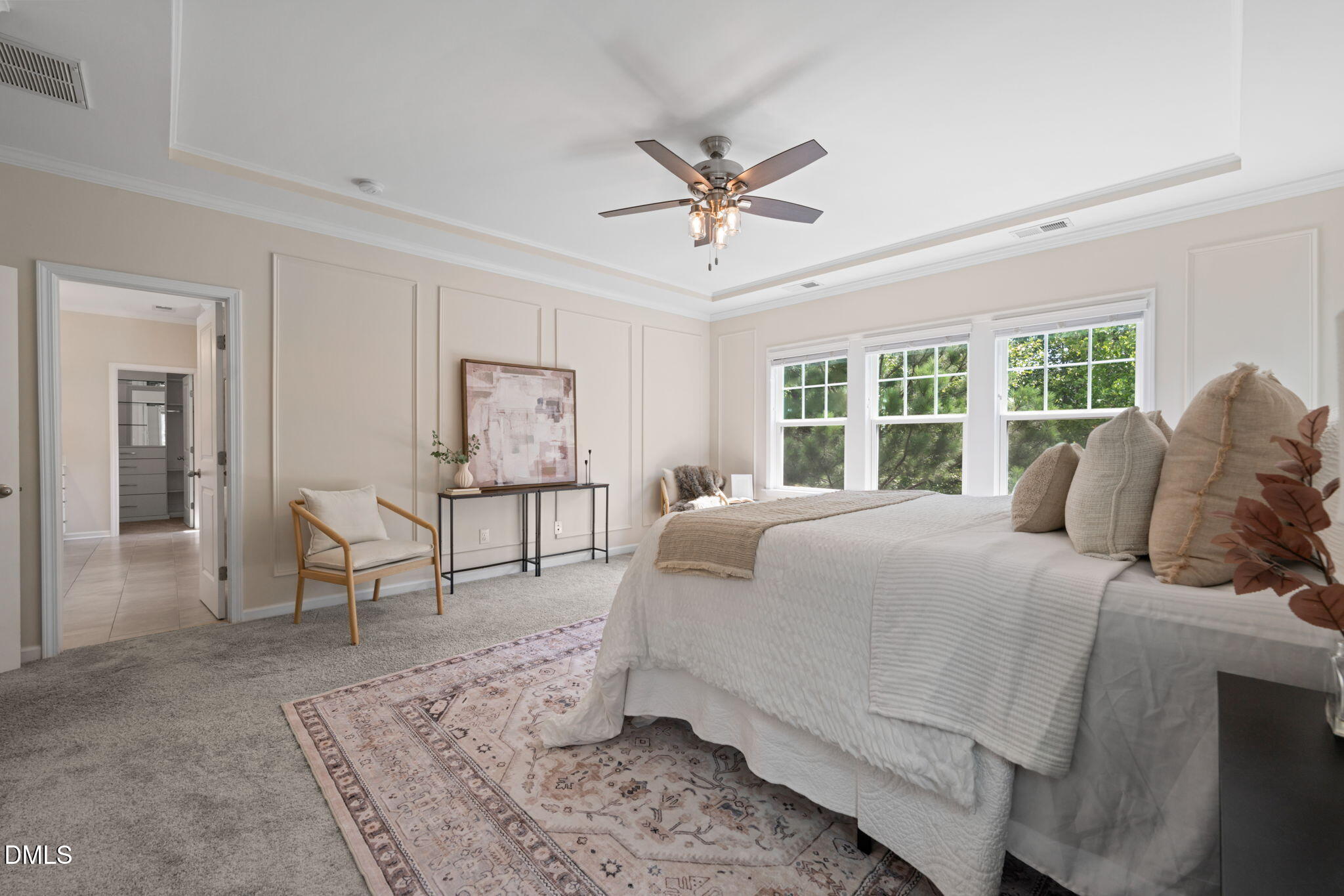 Staged bedroom with a large white bed, patterned rug, and three bright windows.