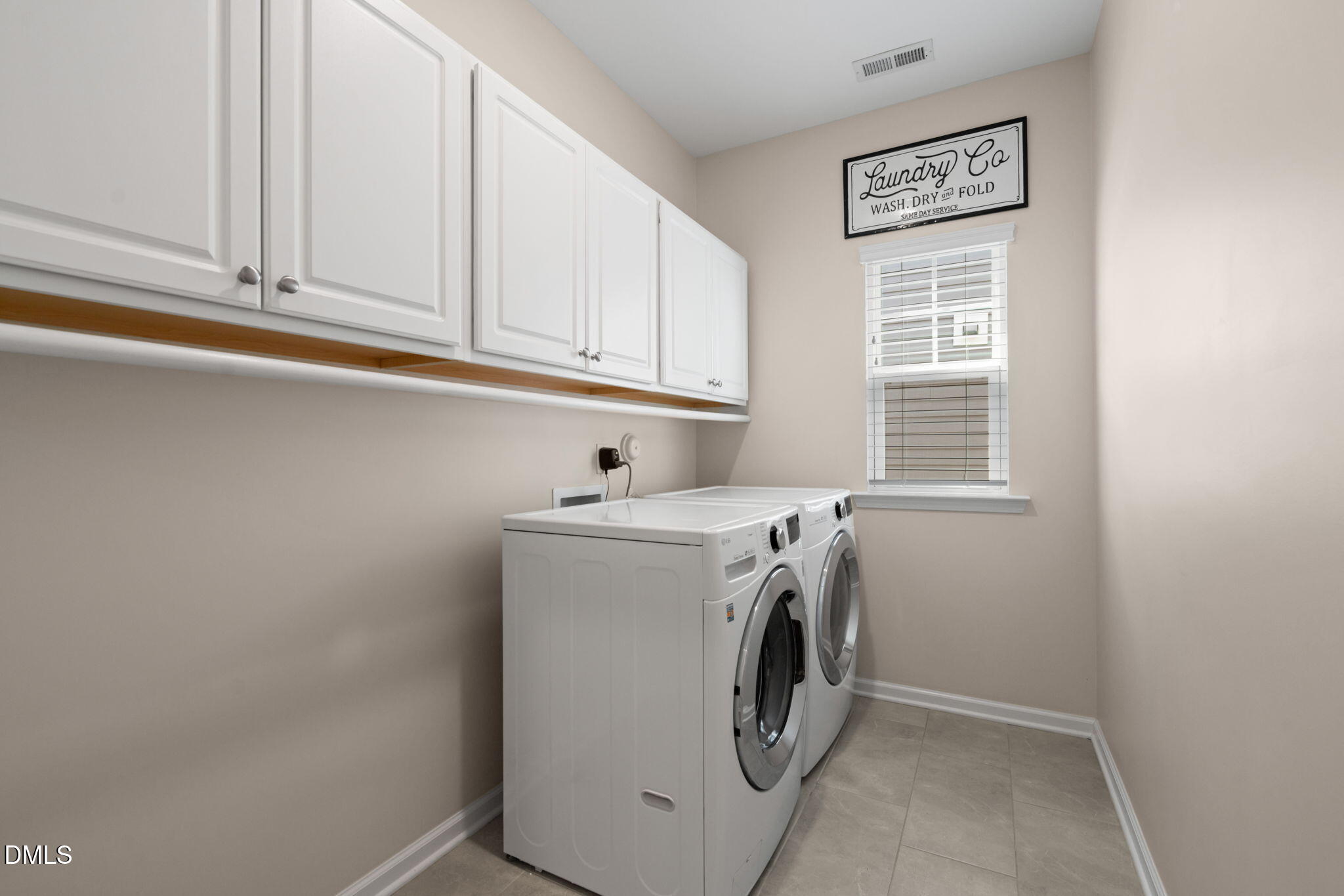 Laundry room with white cabinets, front-loading washer and dryer, gray tile floor, and a window with blinds.