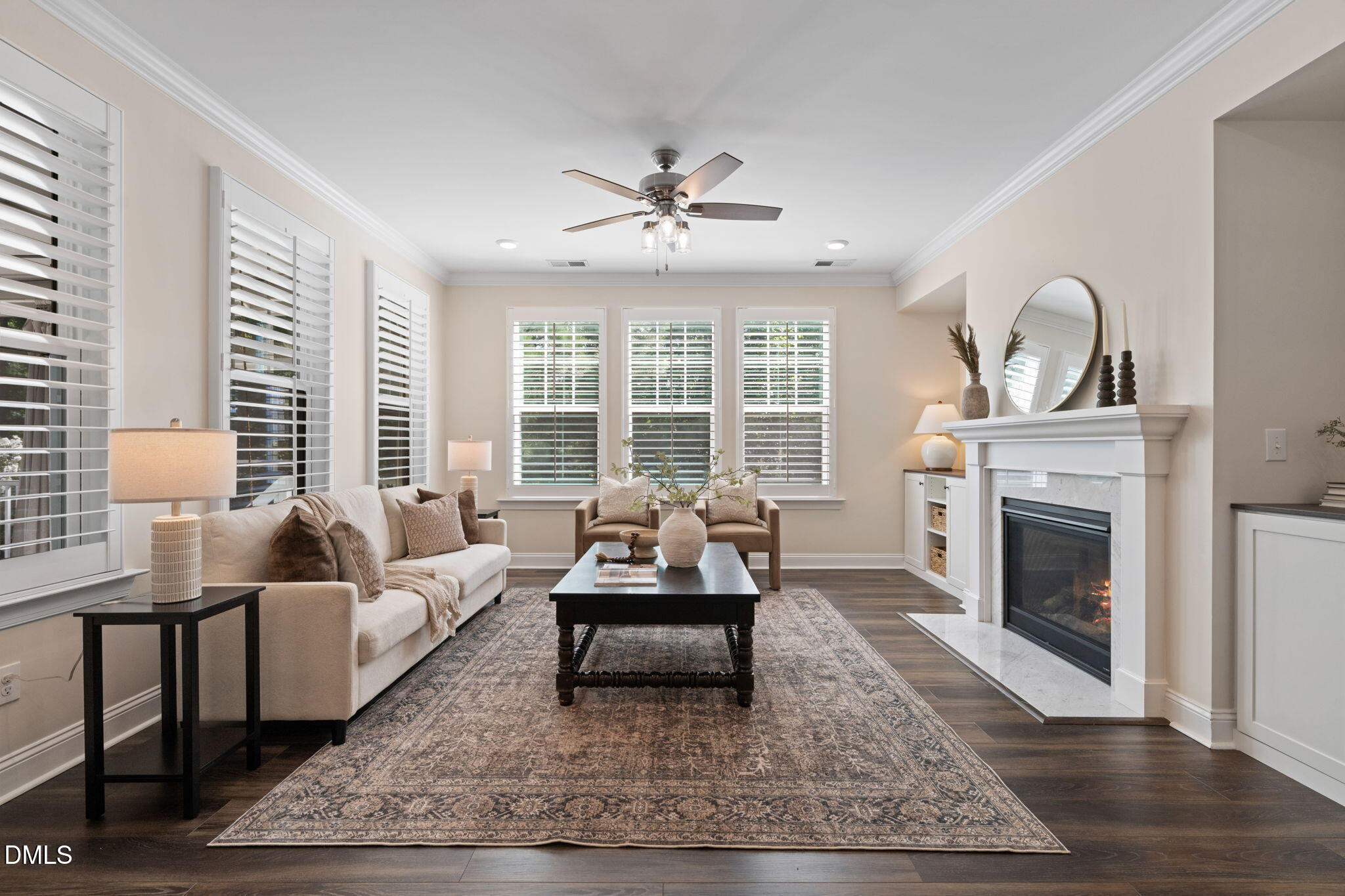 Staged living room with plantation shutters, a white mantel fireplace, and dark hardwood floors.