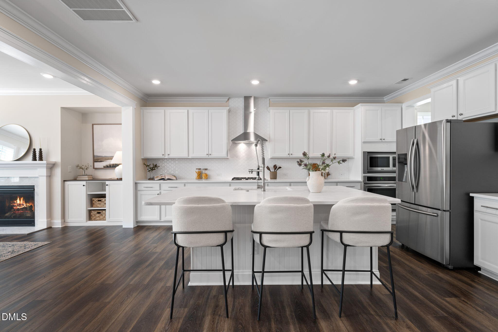 Bright white kitchen with a large island, three bar stools, stainless steel appliances, and dark wood floors.