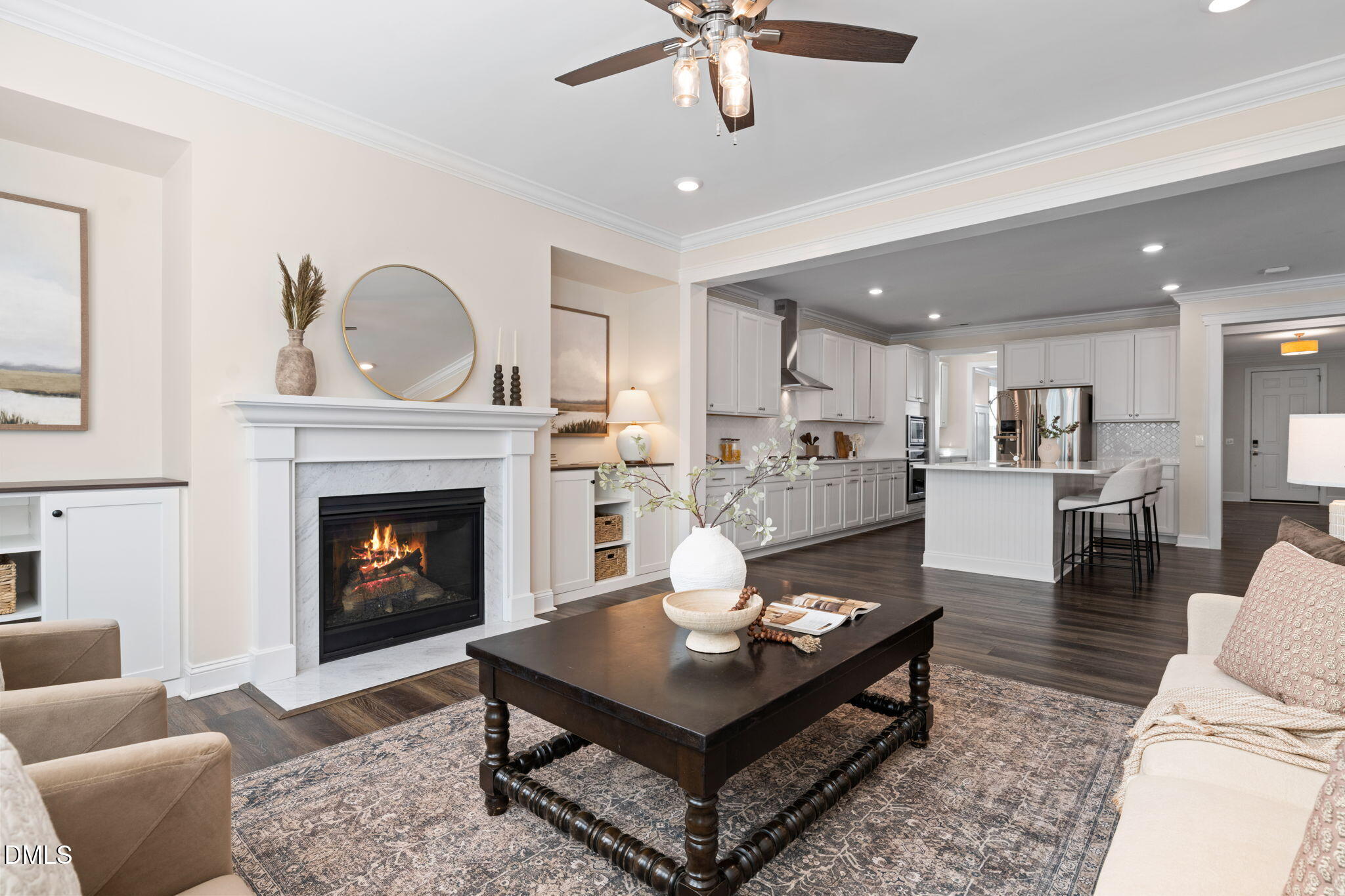 Open-plan living room and kitchen with a white fireplace, dark coffee table, and island seating.