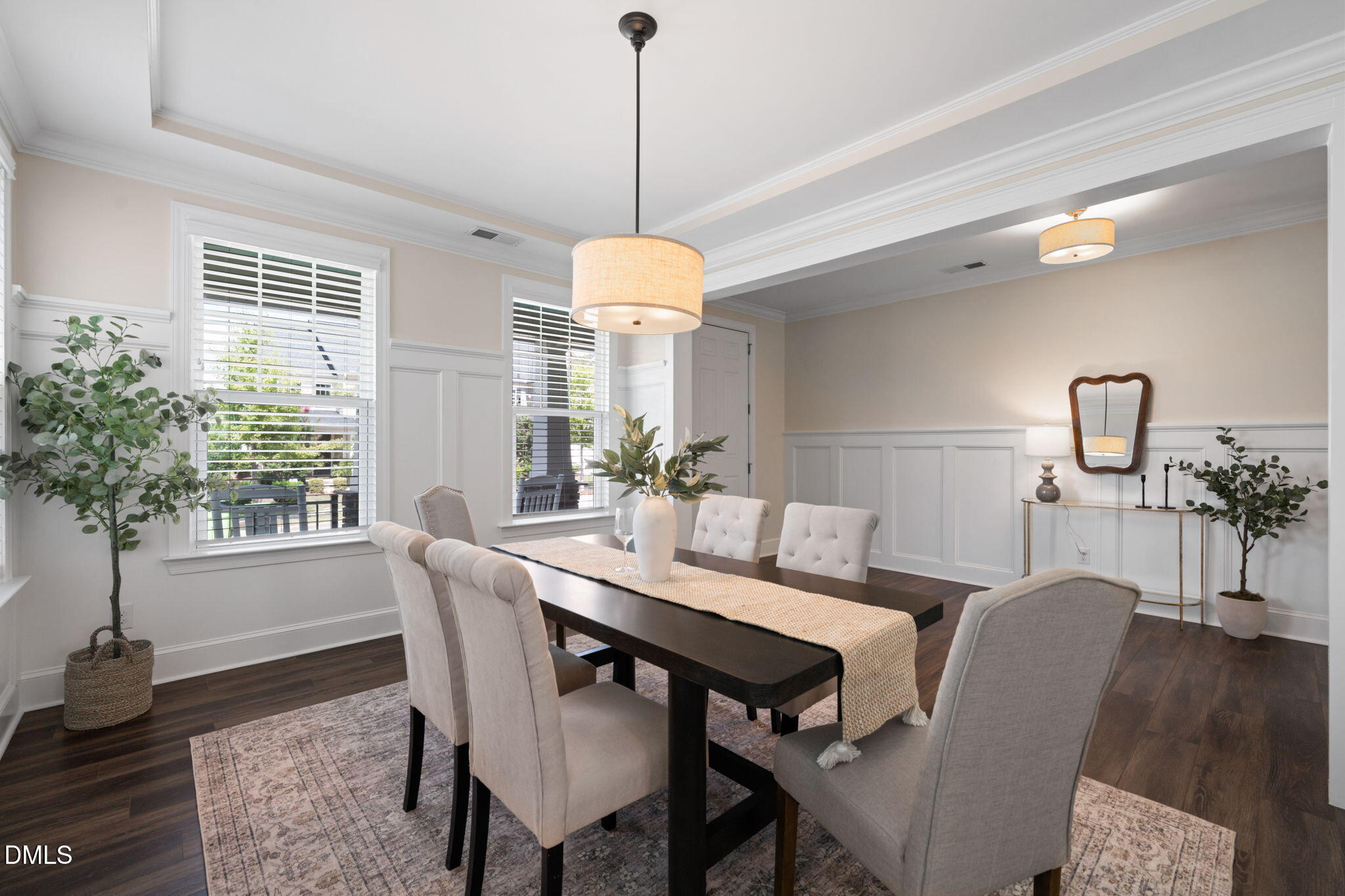 Staged dining room with a dark wood table, upholstered chairs, paneled walls, and large windows.