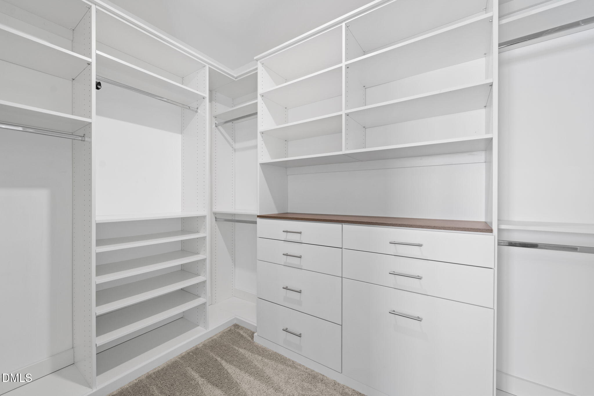 Walk-in closet with white built-in shelving, hanging rods, and drawers beneath a wood-toned countertop.
