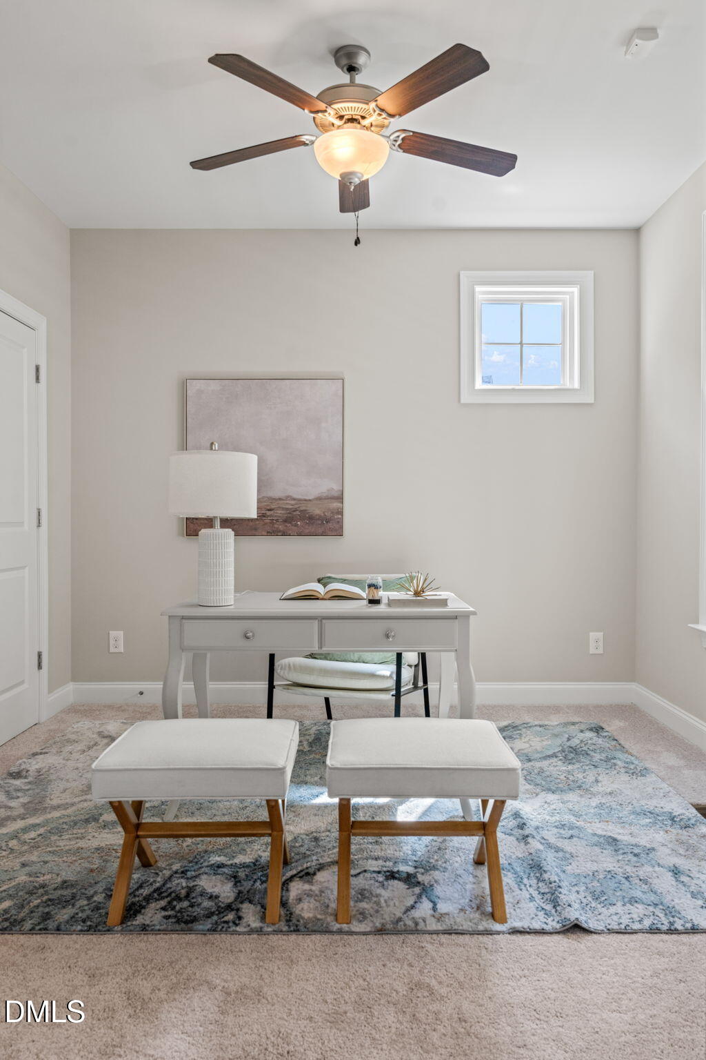 Staged home office with a white desk, upholstered stools, patterned rug, and ceiling fan.