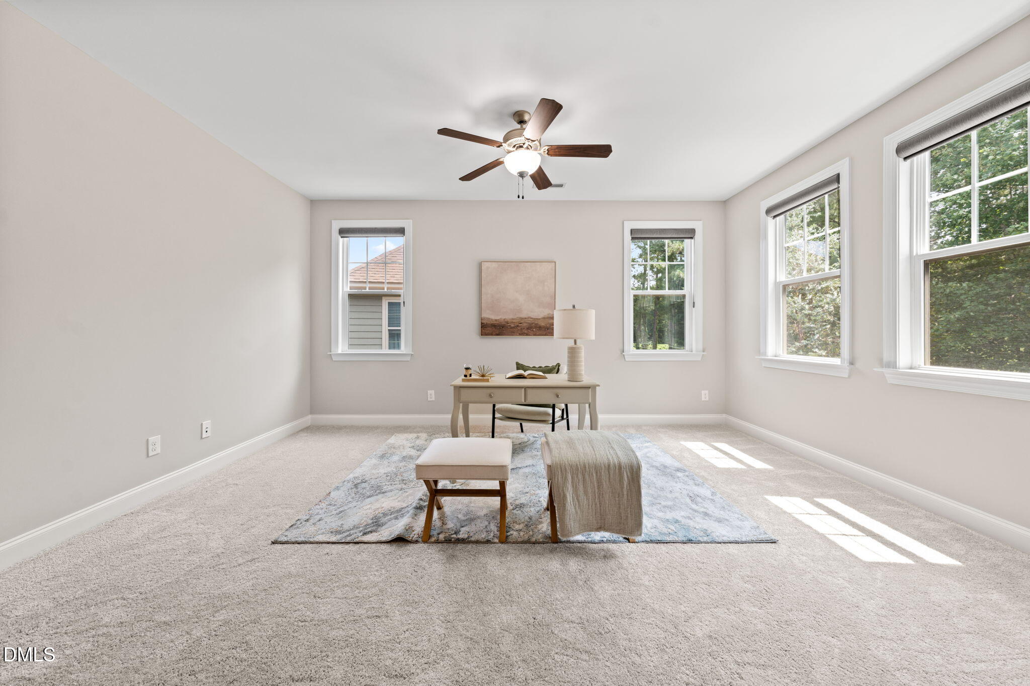 Bright staged office with a desk, patterned rug, ceiling fan, and four windows.