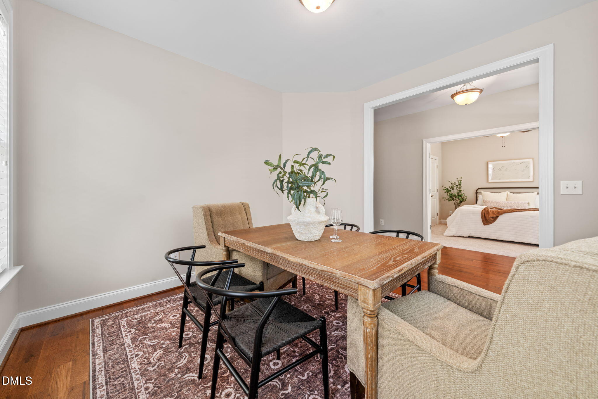 Dining area with a wood table and patterned rug, opening onto a bedroom.