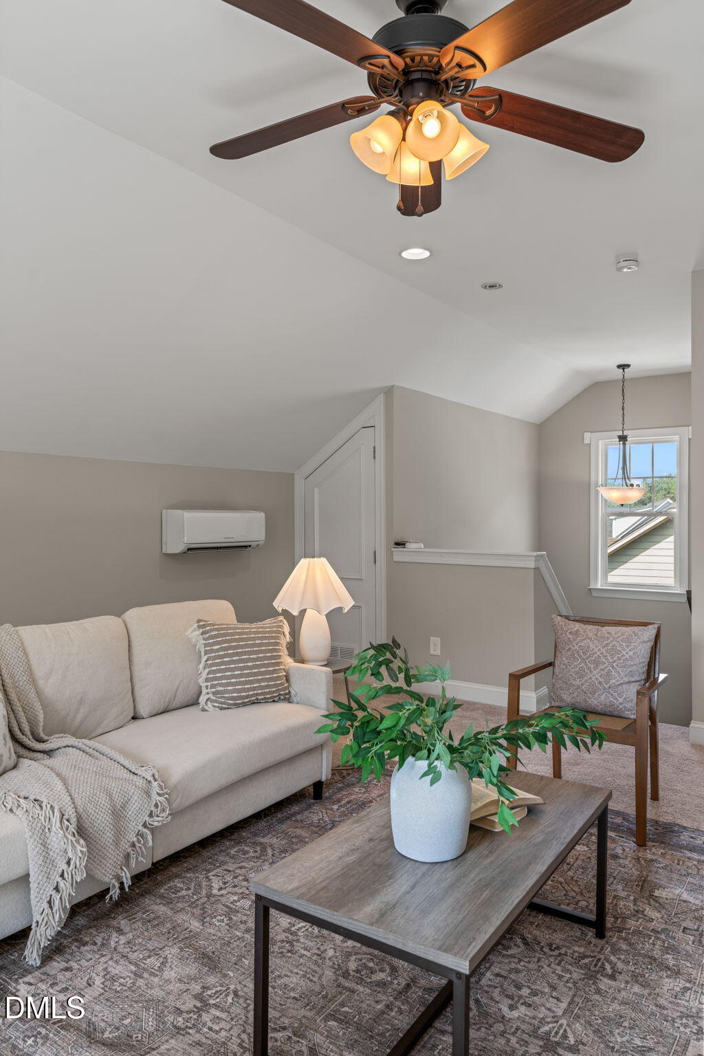 Staged living room with vaulted ceiling, dark wood ceiling fan, beige sofa, and patterned rug.