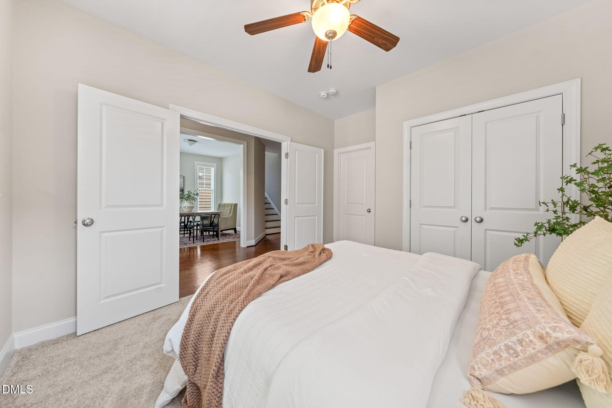 Bedroom with a white bed, blush accents, and open doors to a dining area and hallway.