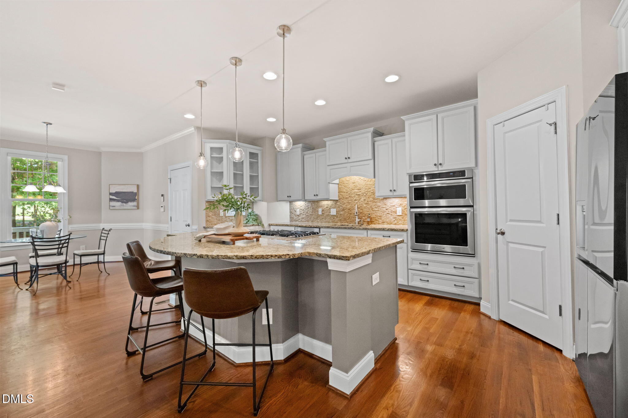Kitchen with a large granite island, white cabinets, stainless steel double ovens, and hardwood floors.