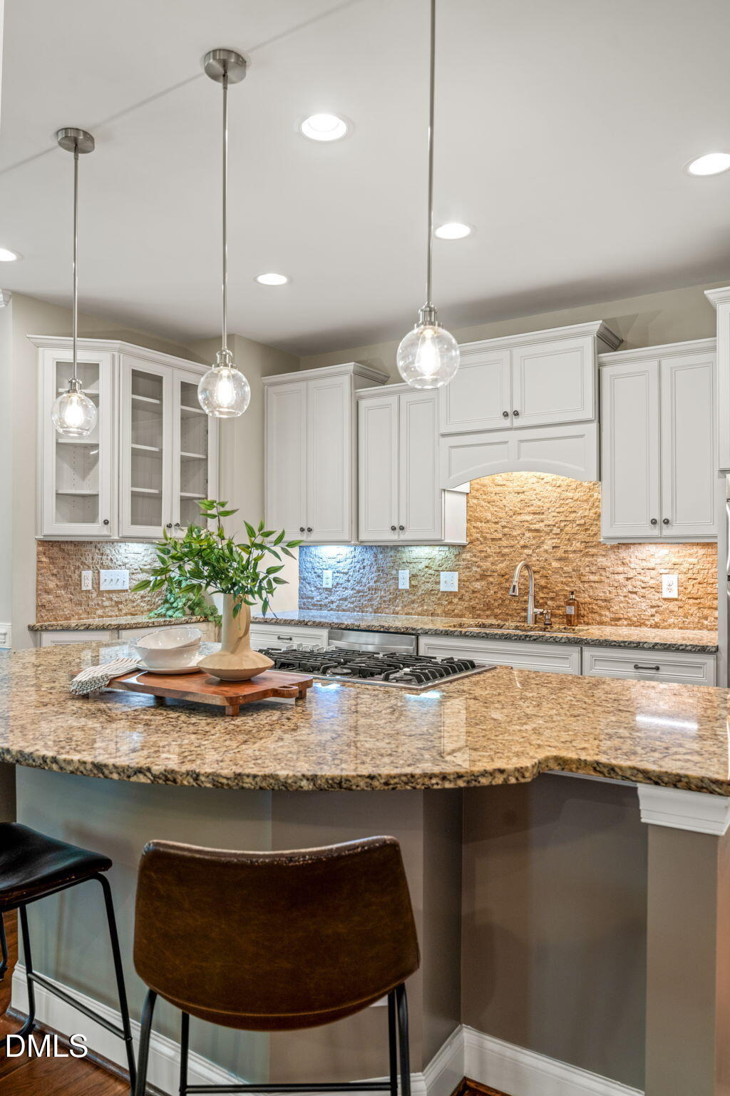 Kitchen with white cabinetry, tan stone backsplash, and a curved granite island with gas cooktop.