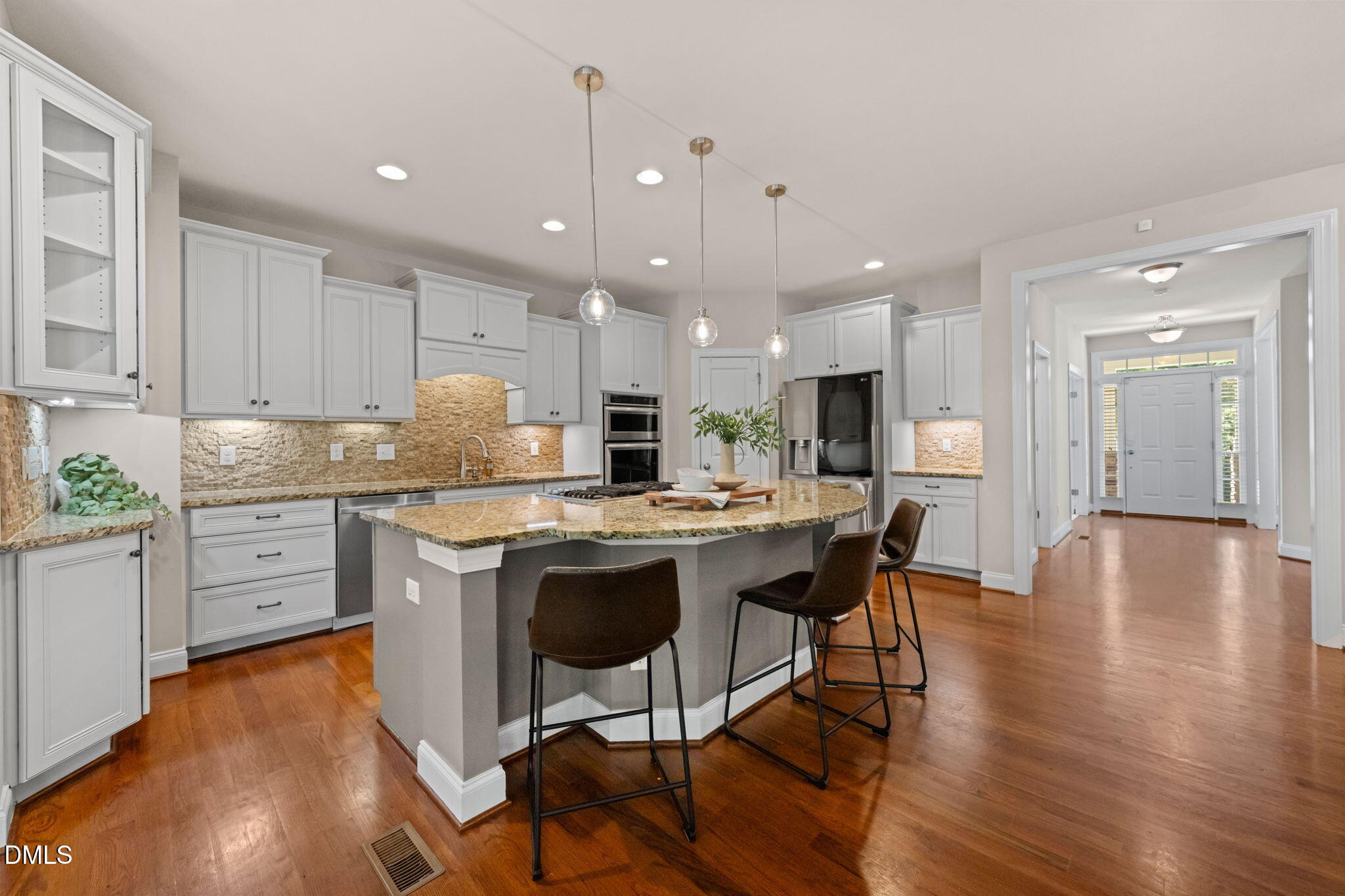 Kitchen with a large granite island, white cabinets, and hardwood floors leading to the front entry.