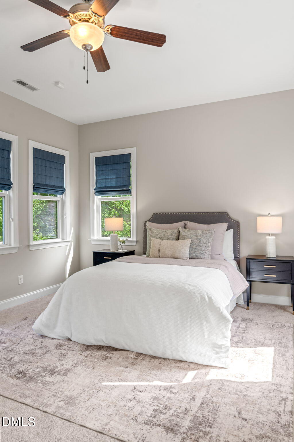 Bedroom with a white bed, gray upholstered headboard, blue Roman shades, and a dark-wood ceiling fan.