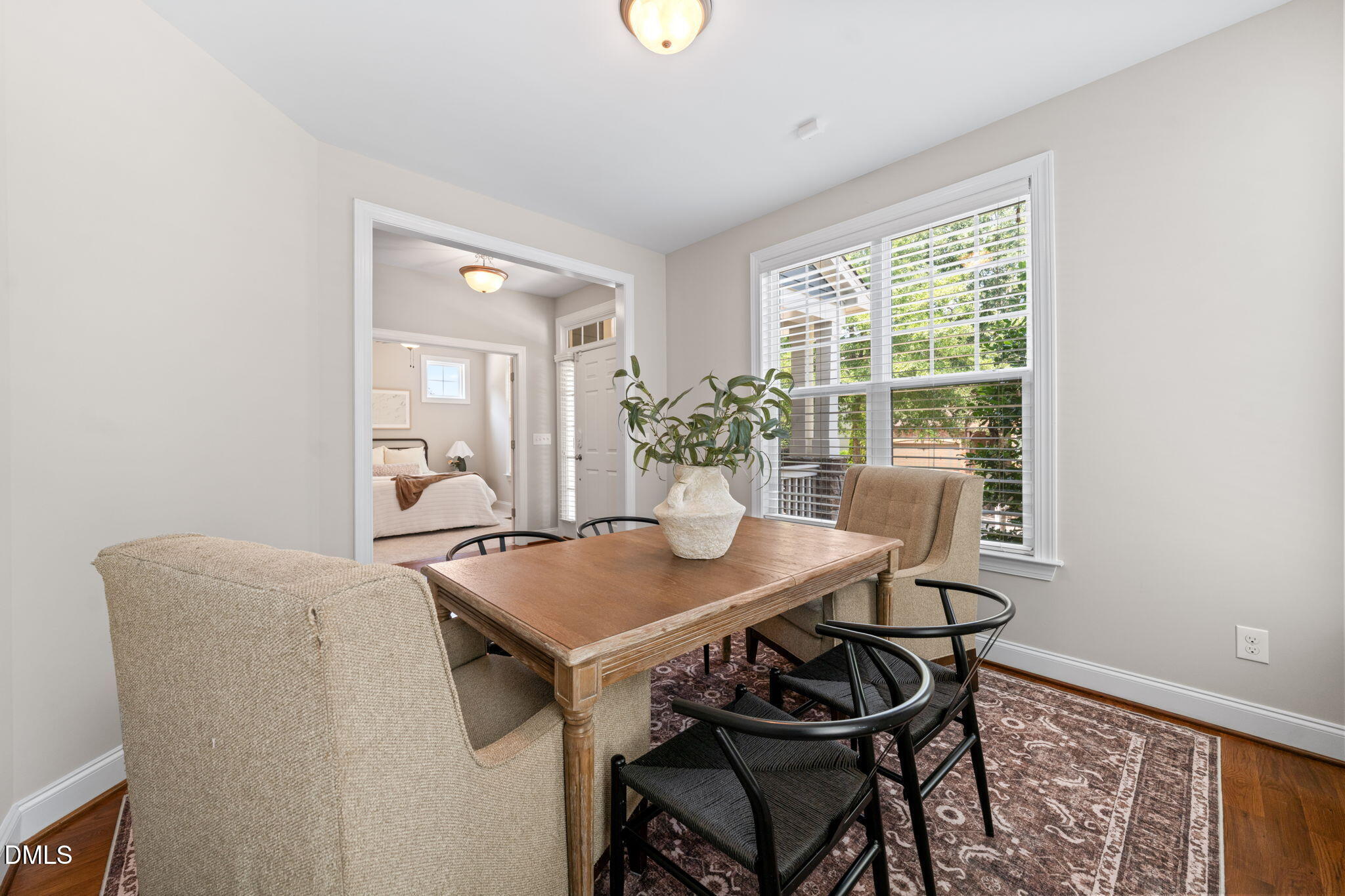 Dining area with a wooden table and large window; bedroom visible through the doorway.