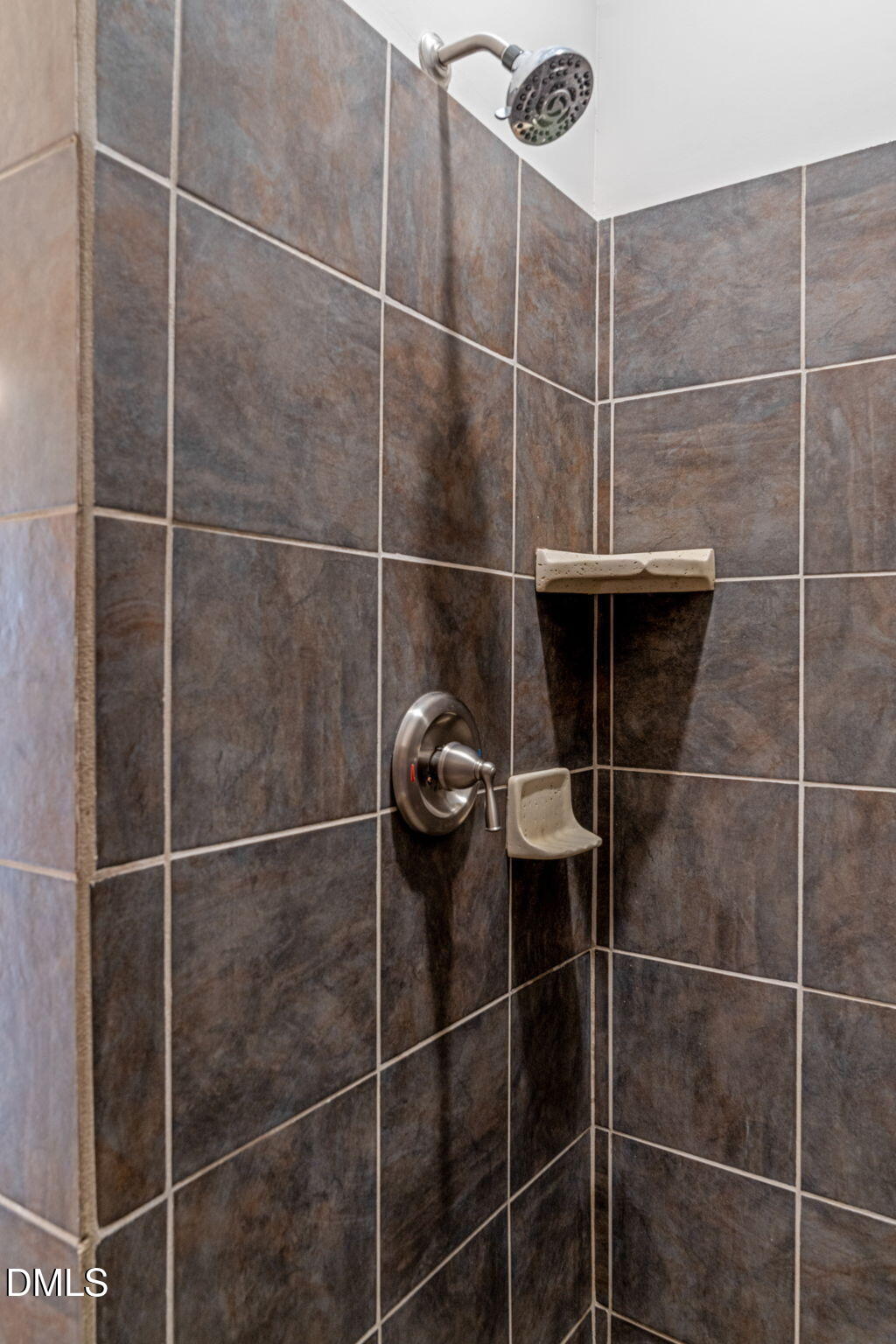 Tiled shower with a chrome showerhead and built-in ceramic soap dishes.