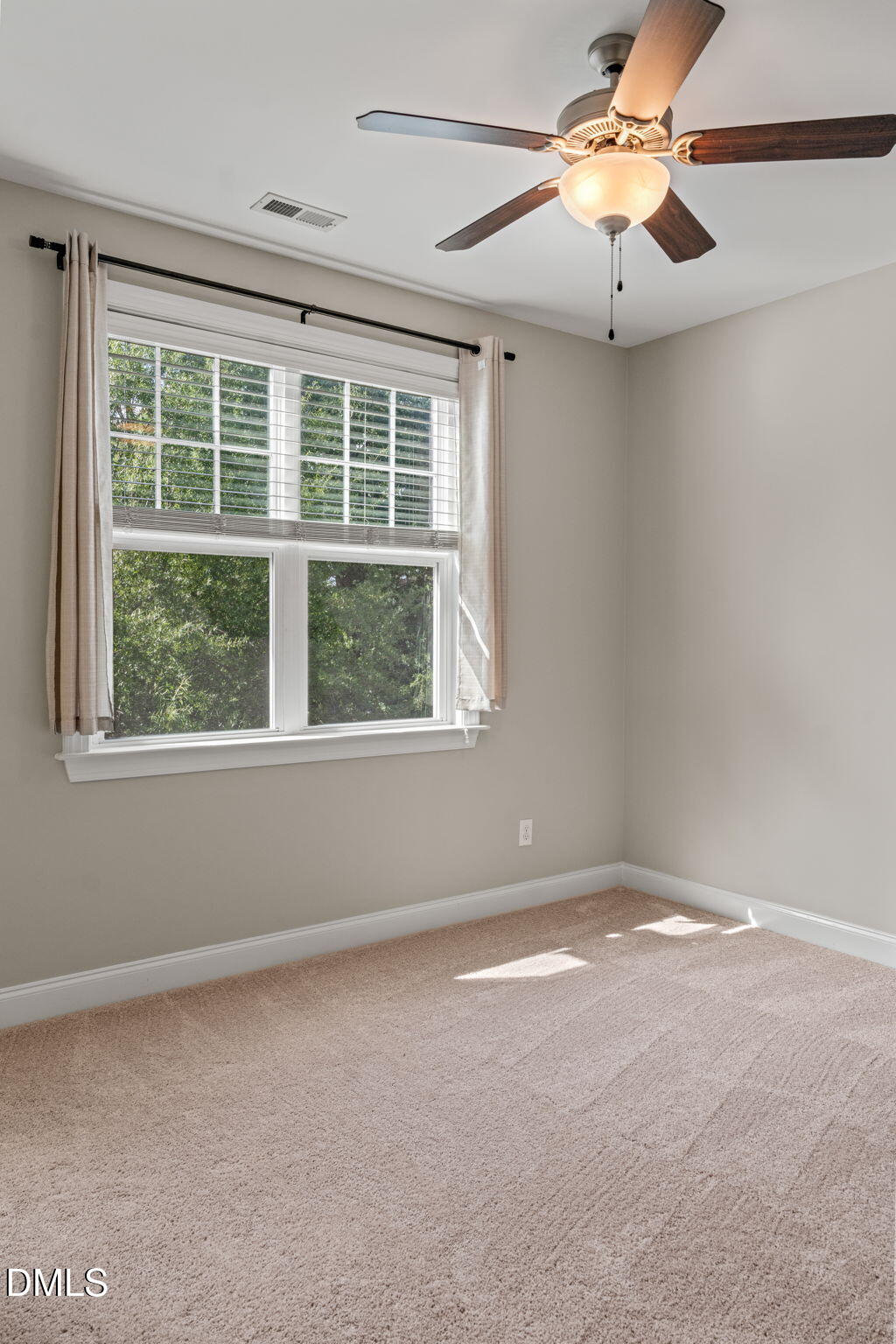 Empty carpeted bedroom with a large curtained window and lit ceiling fan.