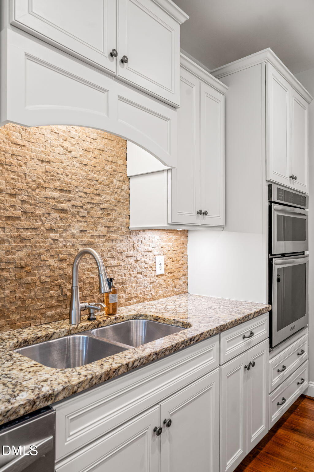Kitchen with white cabinetry, a stacked-stone backsplash, granite counters, and a stainless steel double sink.