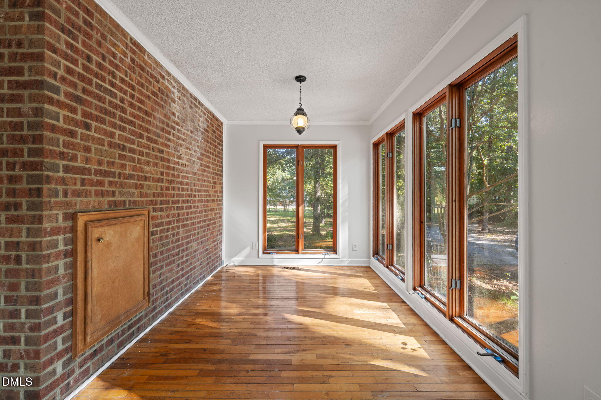 Sunroom with a brick wall, hardwood floors, and tall windows overlooking trees.