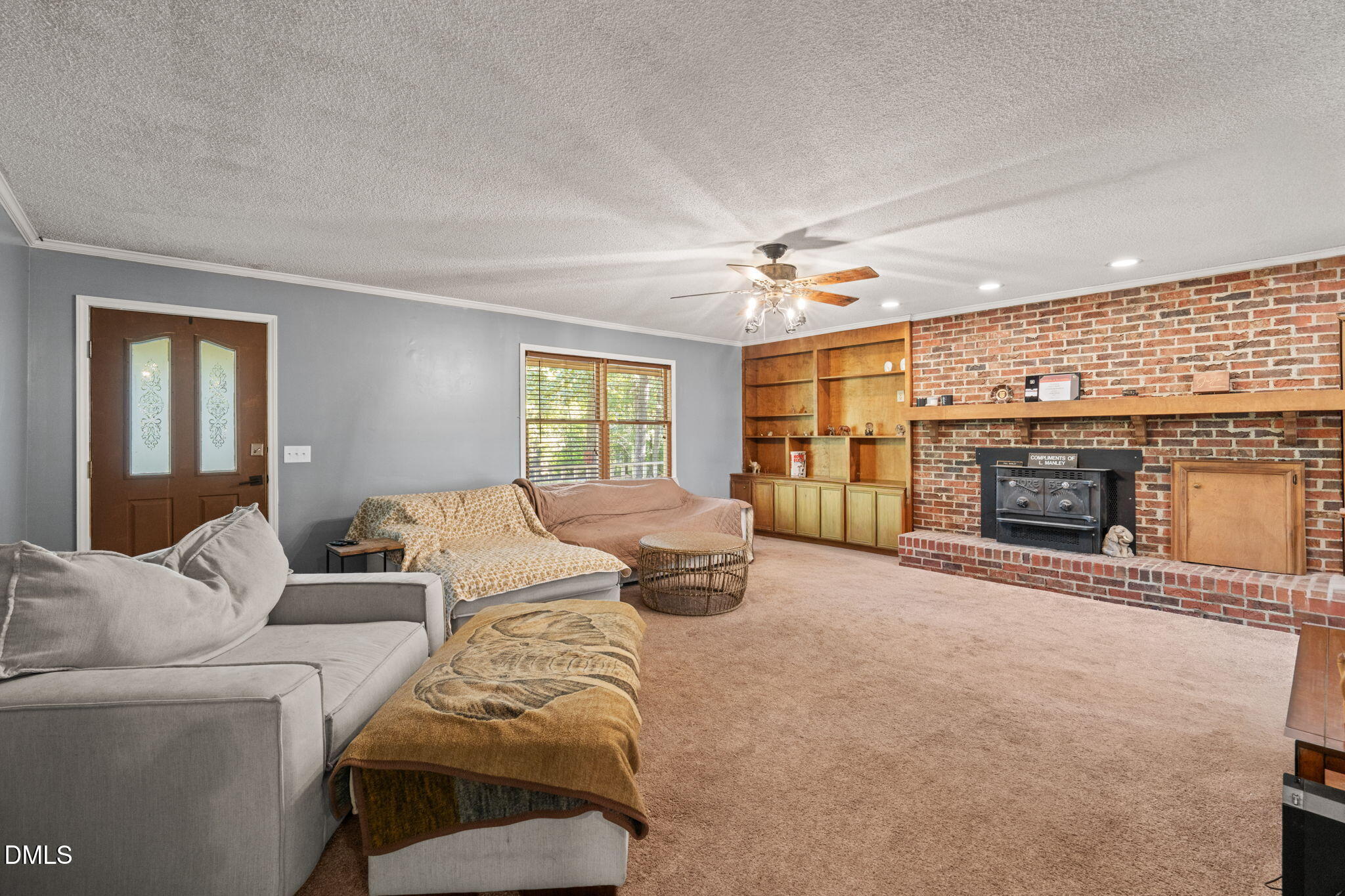 Furnished living room with a brick fireplace, wood-burning stove, and built-in wooden shelving.