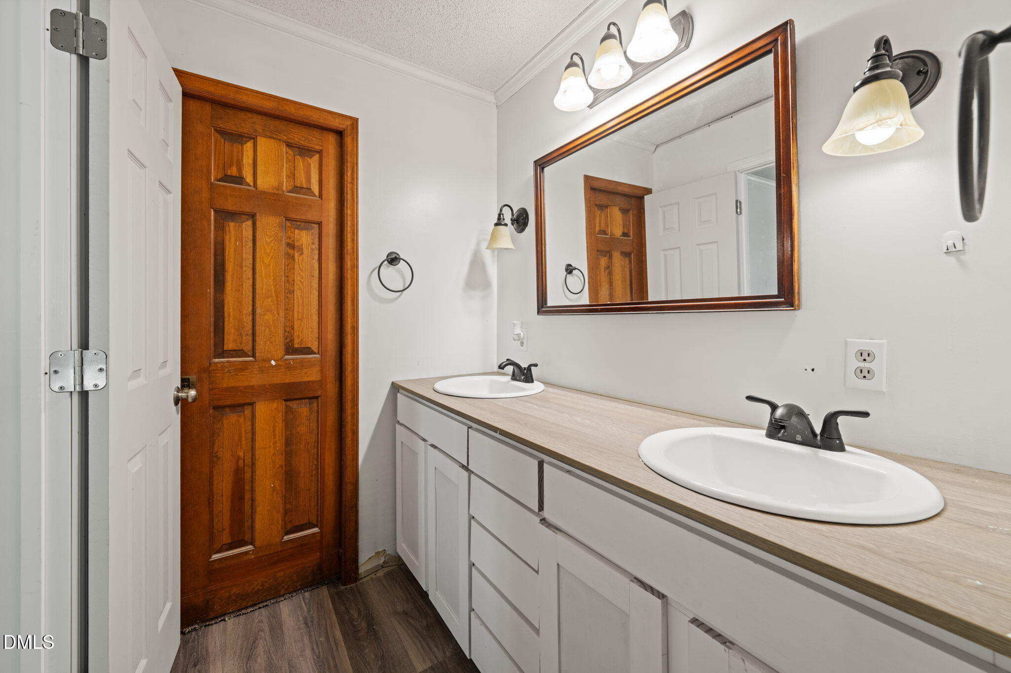 Bathroom with a double-sink vanity, large framed mirror, and dark wood paneled door.