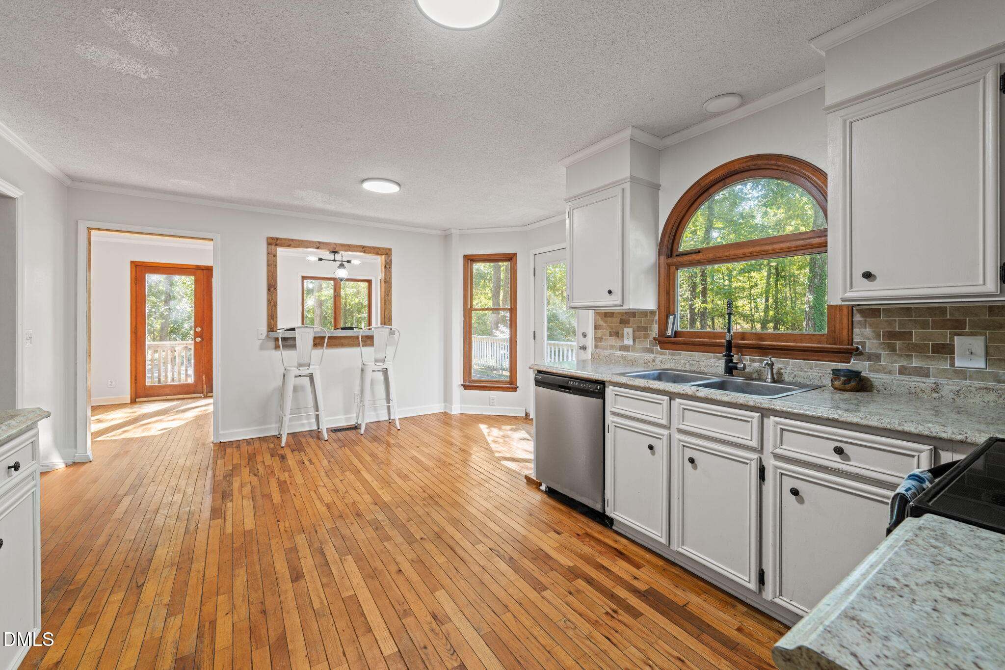 Kitchen with hardwood floors, white cabinets, granite counters, and a large arched window above the sink.
