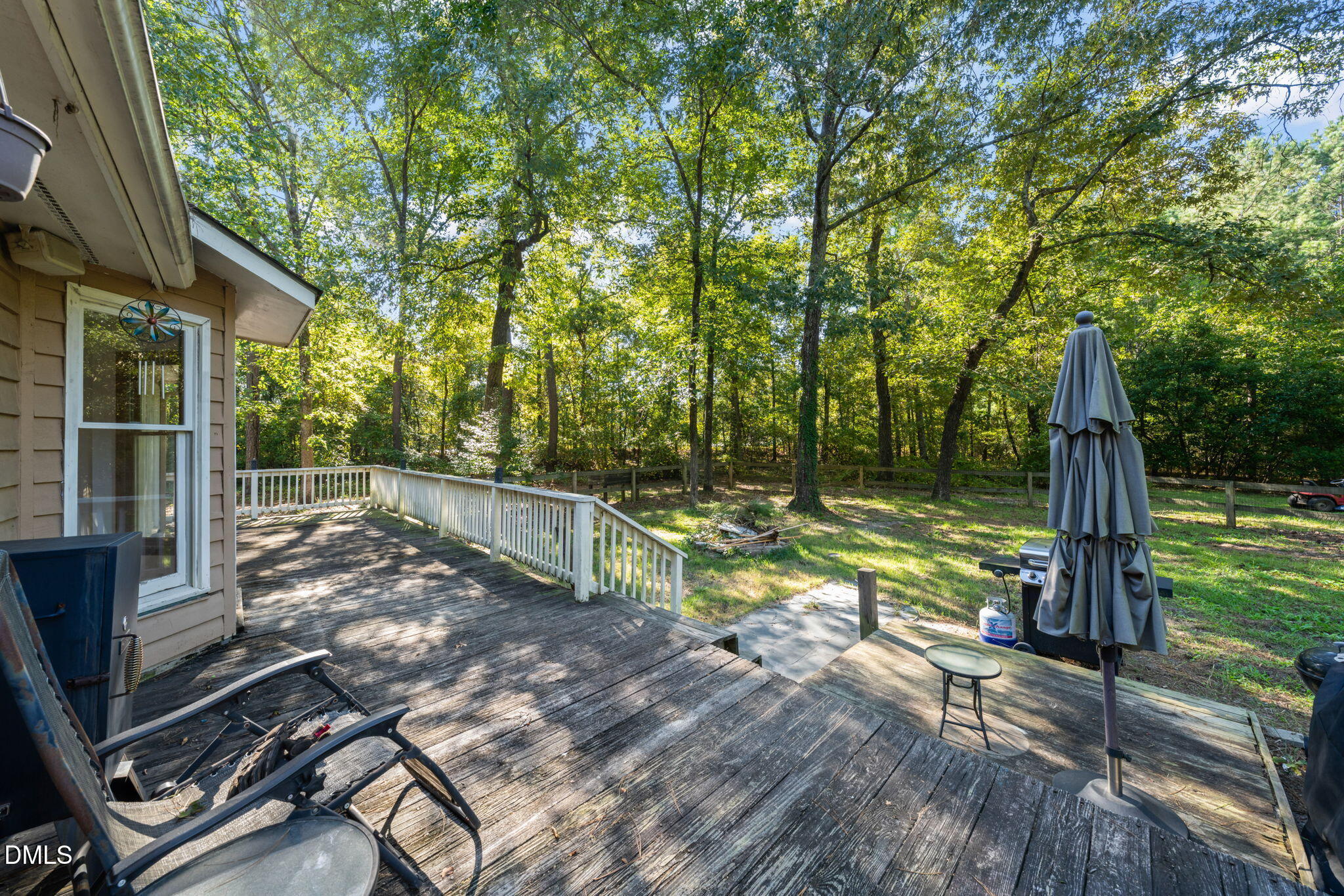 Wood deck with lounge chairs and a closed umbrella overlooking a fenced, wooded backyard.