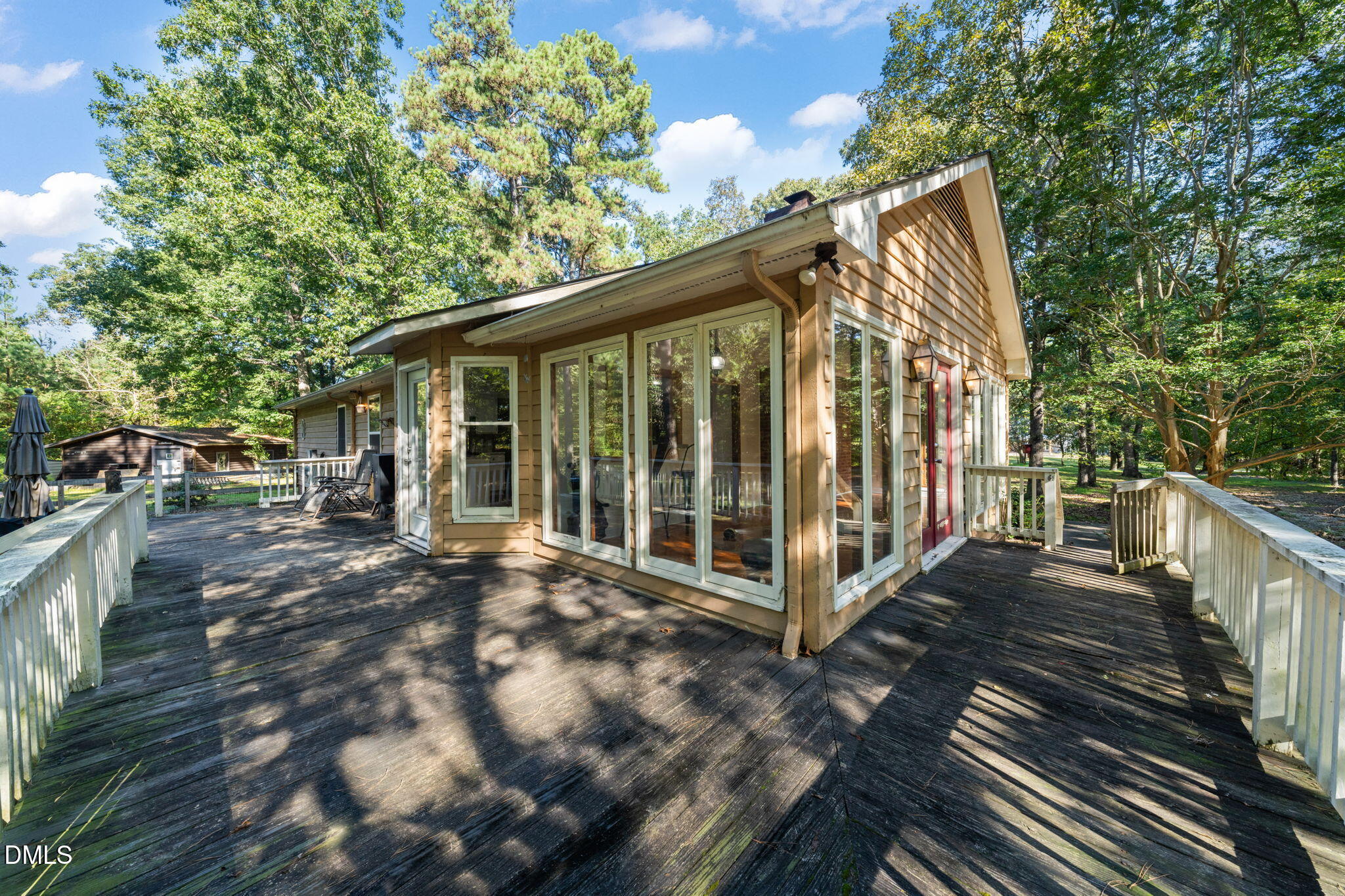 Home’s rear exterior with a broad wood deck, expansive glass doors, and mature trees.