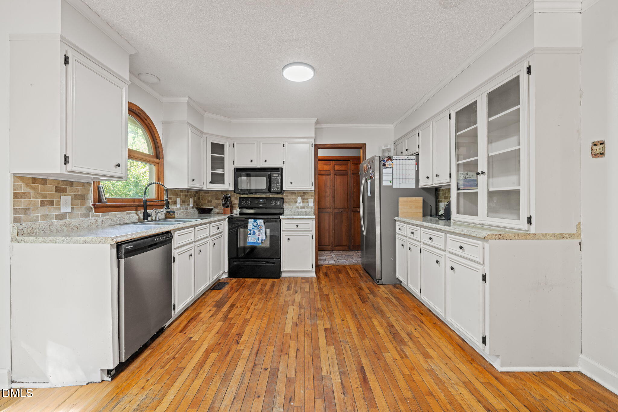 Kitchen with white cabinets, granite counters, hardwood floors, and an arched window over the sink.