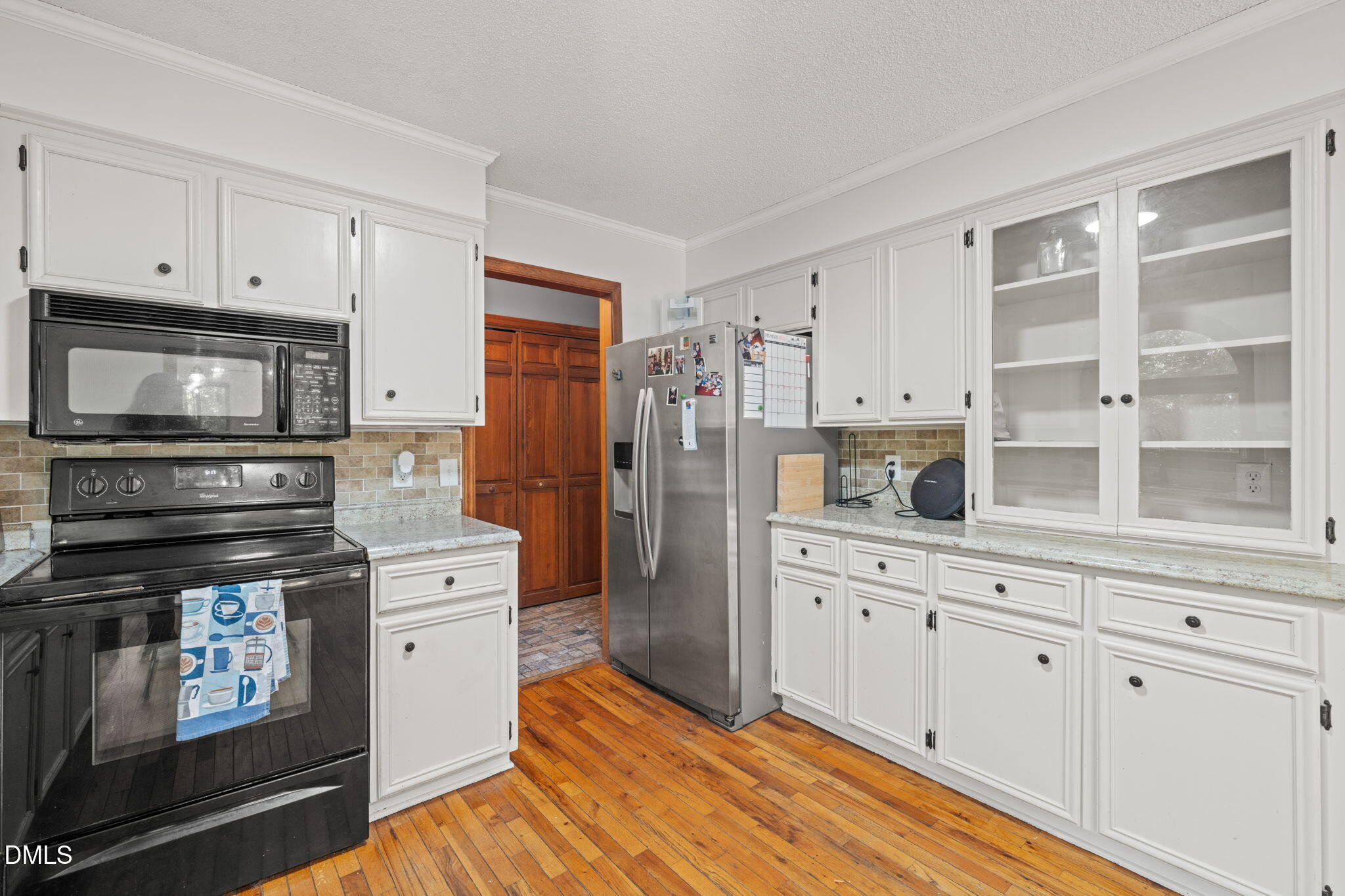 Kitchen with white cabinetry, stainless steel refrigerator, black range, and warm wood floors.