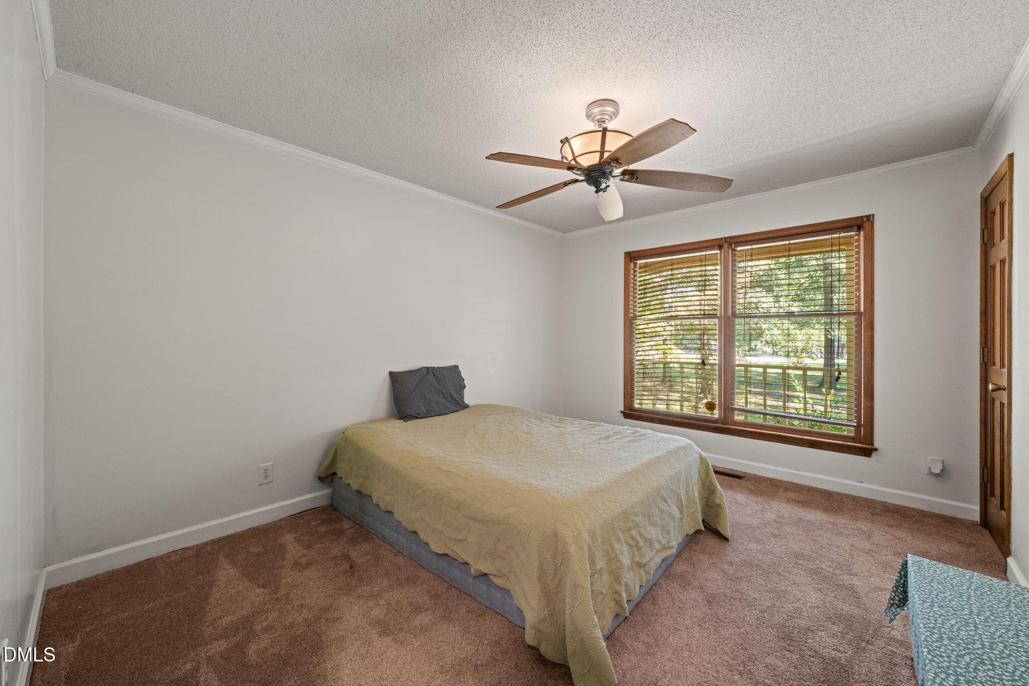Bedroom with a quilt-covered bed, ceiling fan, and large wood-trimmed window overlooking greenery.