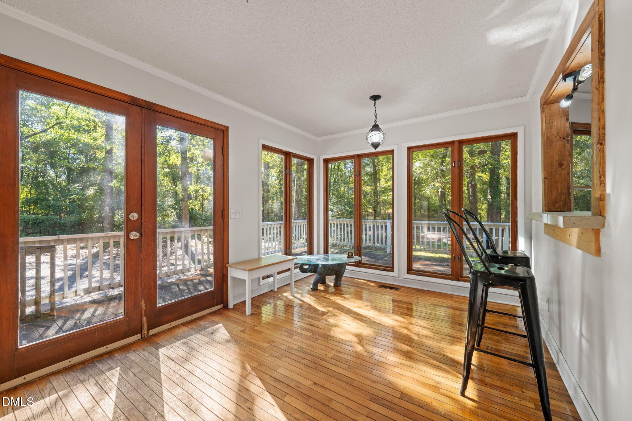 Sunroom with wood-framed glass doors, hardwood floors, and views of trees and the deck.