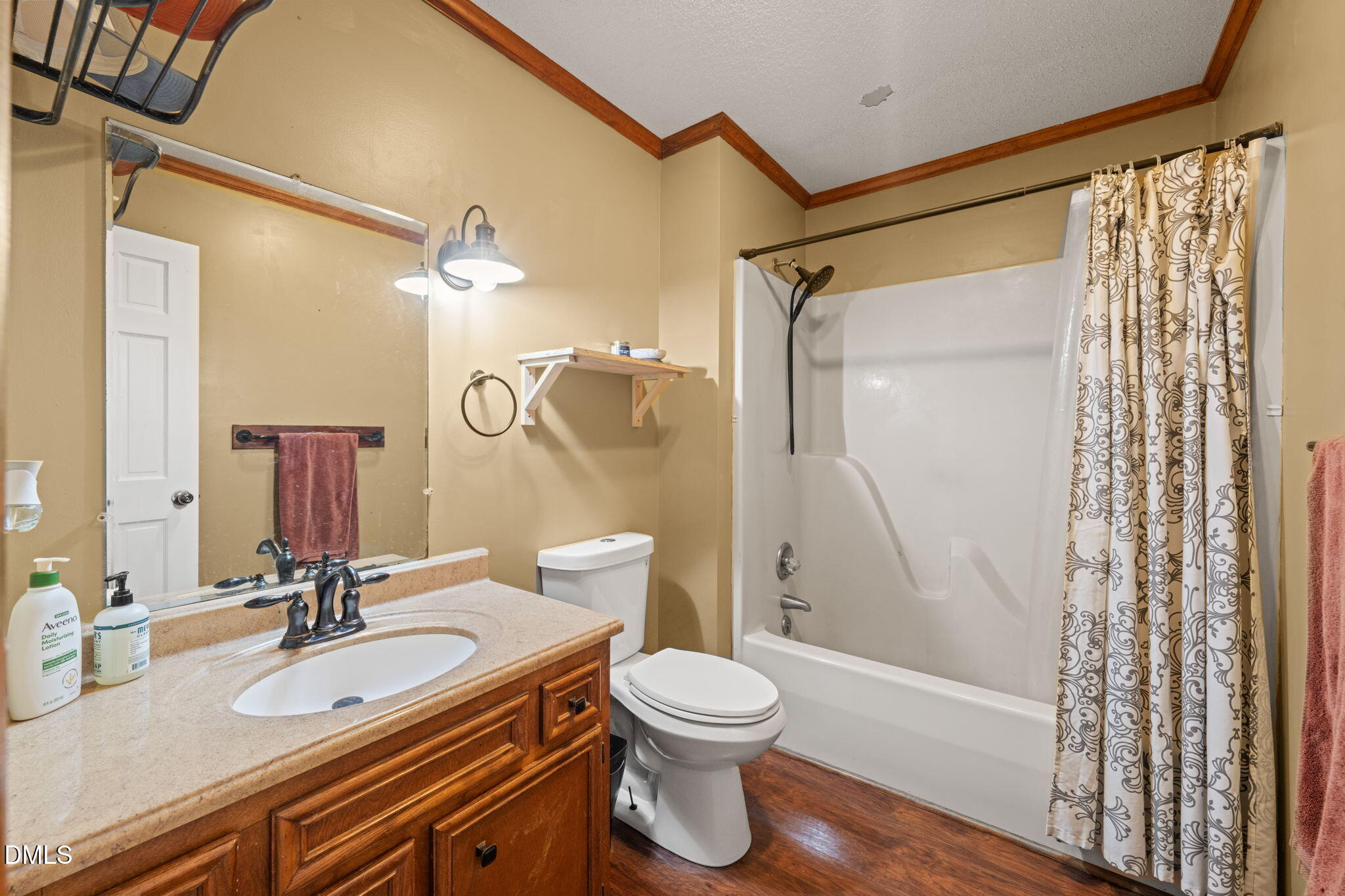 Bathroom with a wood vanity, white tub-shower, patterned curtain, and wood-look flooring.