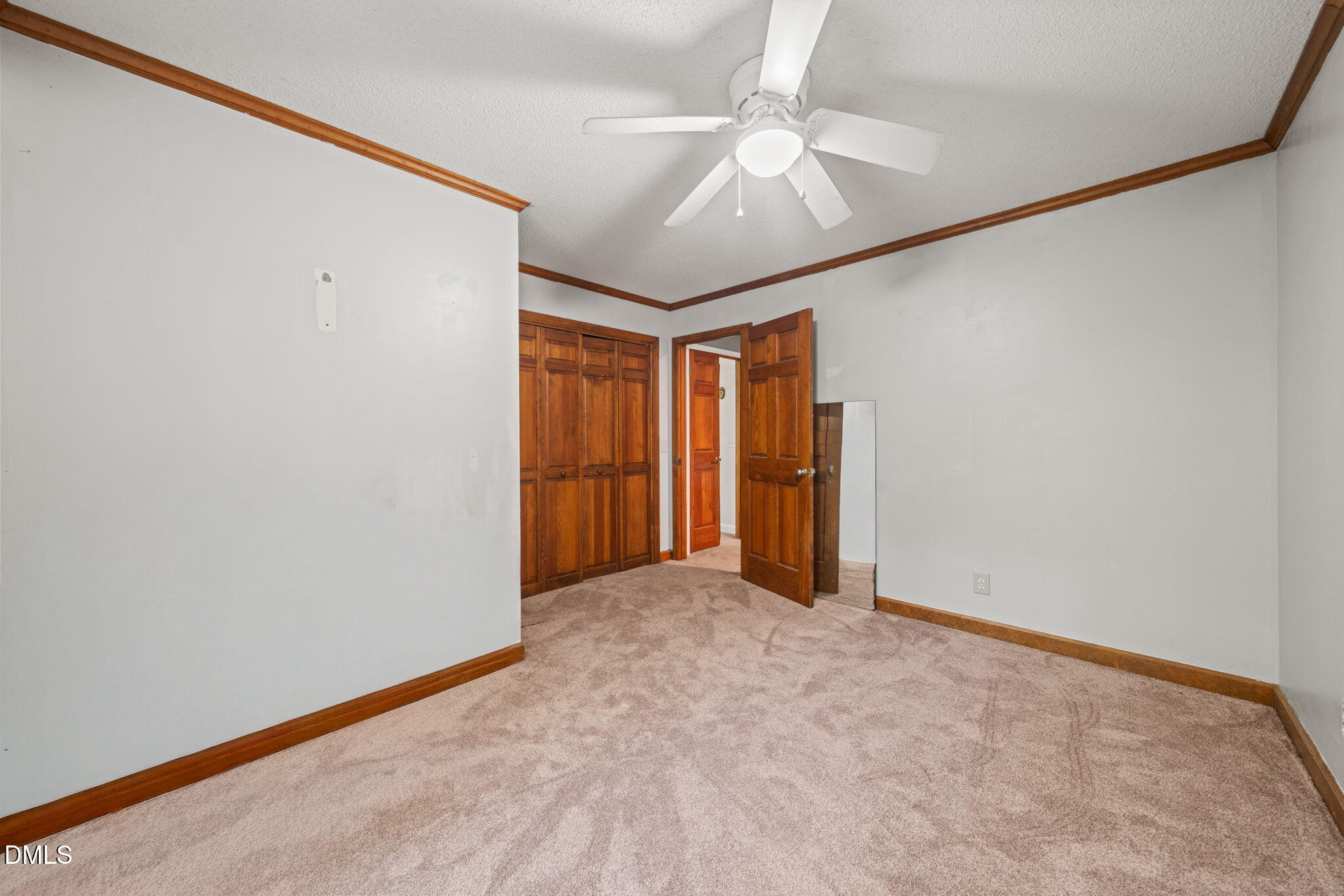 Empty carpeted room with wooden closet doors, an open doorway, and a ceiling fan.
