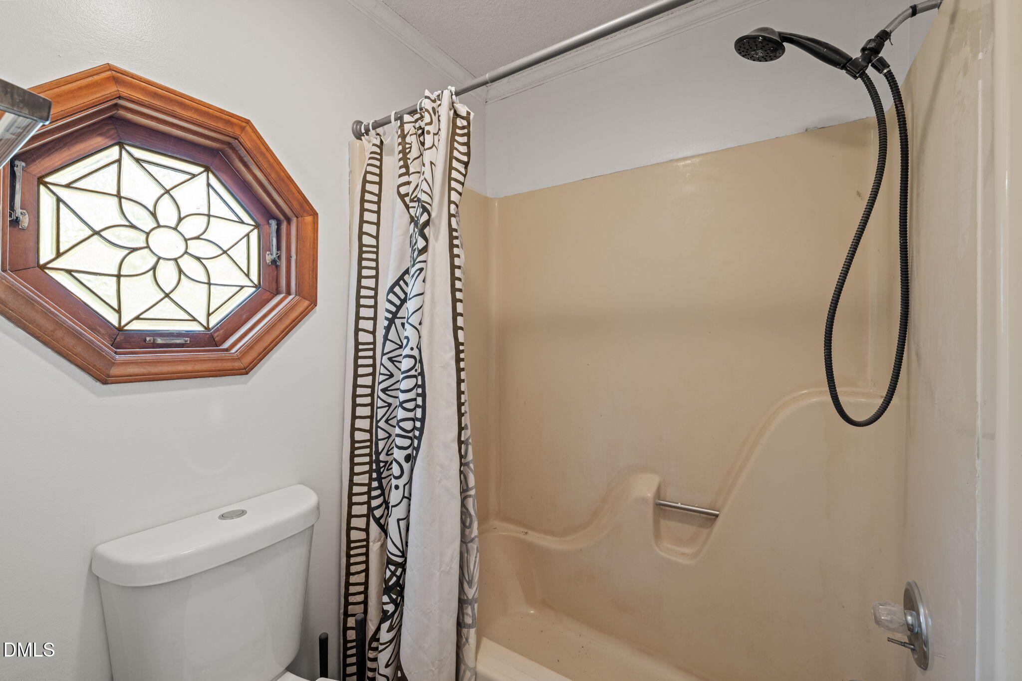 Bathroom shower and toilet beside an octagonal wood-framed window with decorative glass.