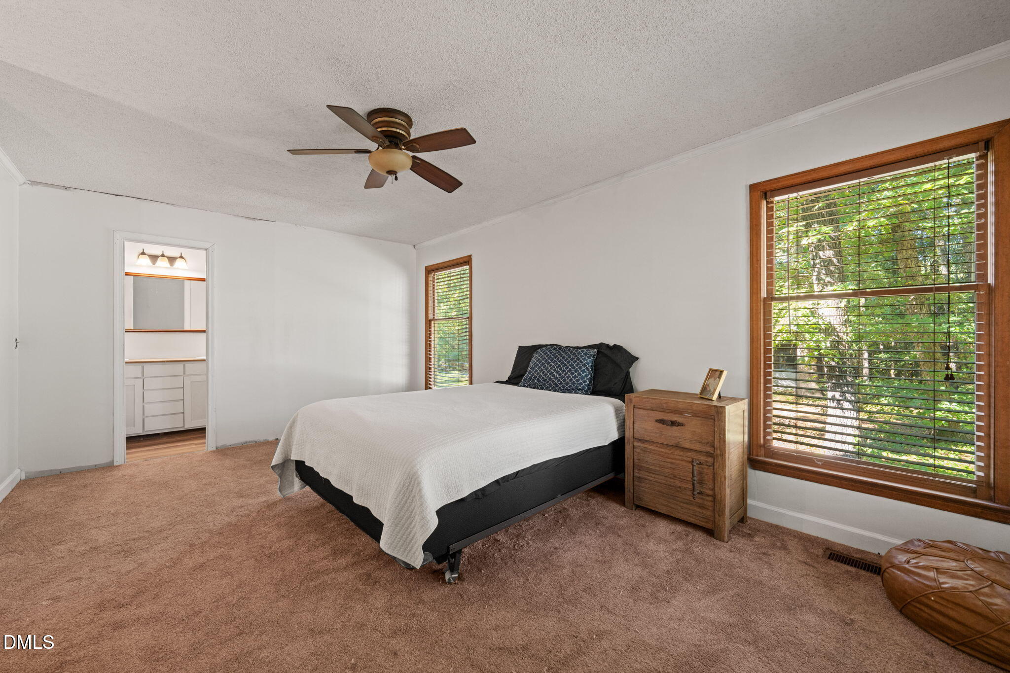 Bedroom with a white-covered bed, wood-trimmed windows, and a doorway to the bathroom.