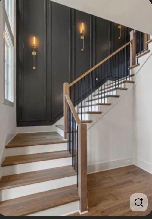 Curved staircase with wood treads, black balusters, and a dark paneled wall with sconces.
