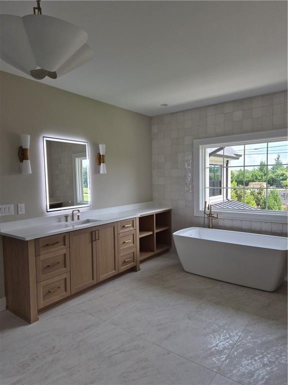 Bathroom with a freestanding tub, wood vanity, and large window.